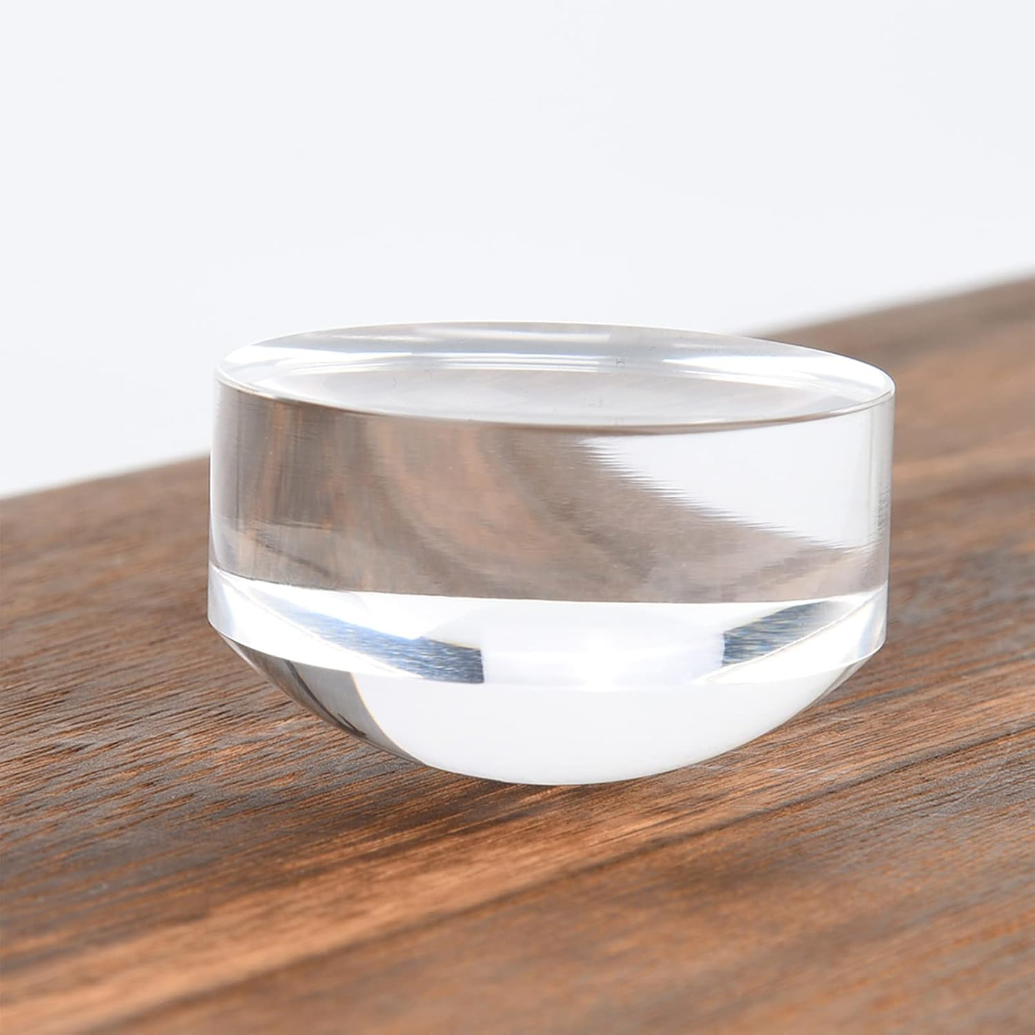 Ein transparenter Acrylzylinder mit abgerundetem Boden auf einer Holzoberfläche.