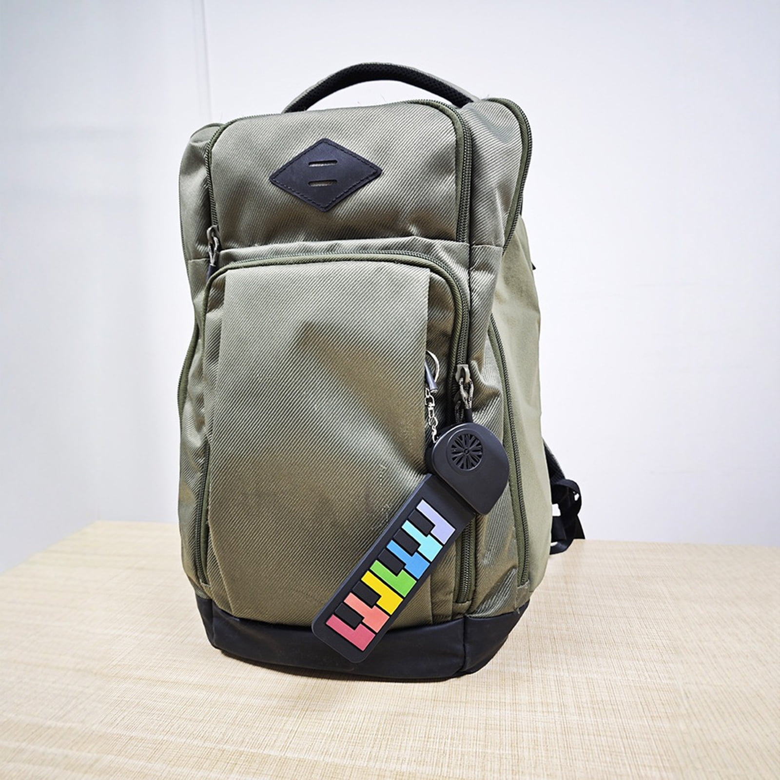 Ein grüner Rucksack mit schwarzem Boden und bunten Streifen am Reißverschluss steht auf einem Holztisch.
