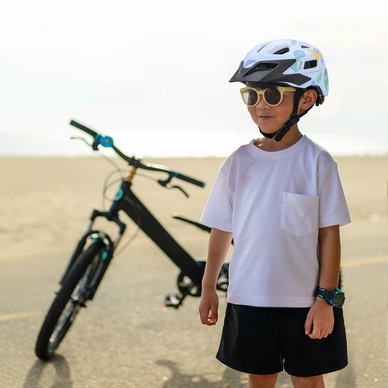 Un bambino con casco e occhiali da sole si trova all'aperto con una bicicletta.