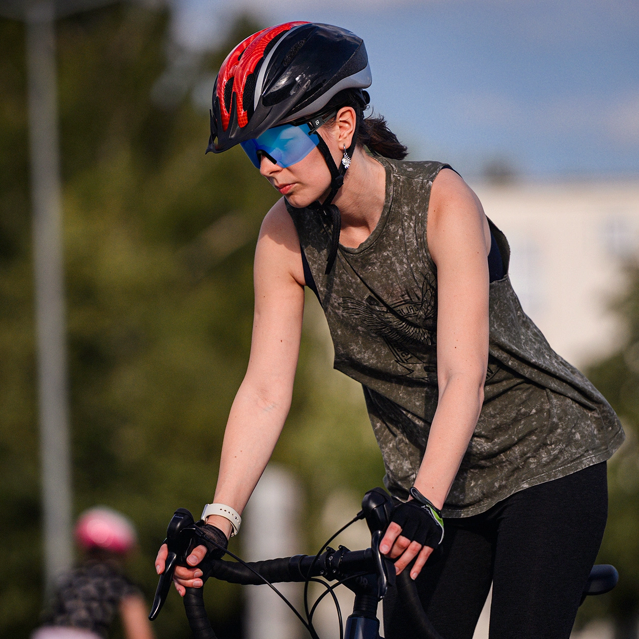 Una ciclista con casco nero e rosso, occhiali da sole blu e canotta verde va in bicicletta.