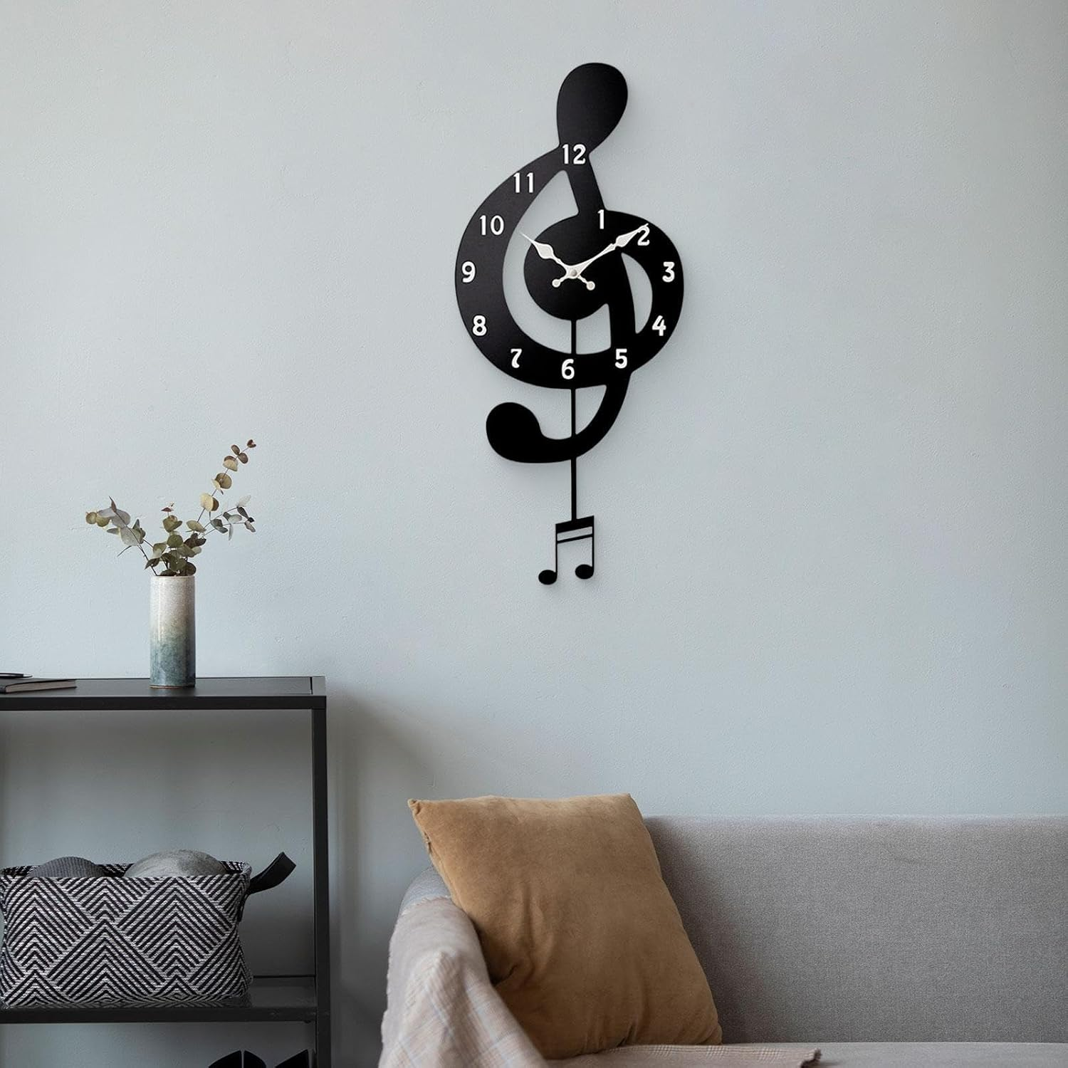 Eine schwarze Notenschlüssel-Wanduhr hängt über einem grauen Sofa mit braunem Kissen, neben einem Regal mit Vase.