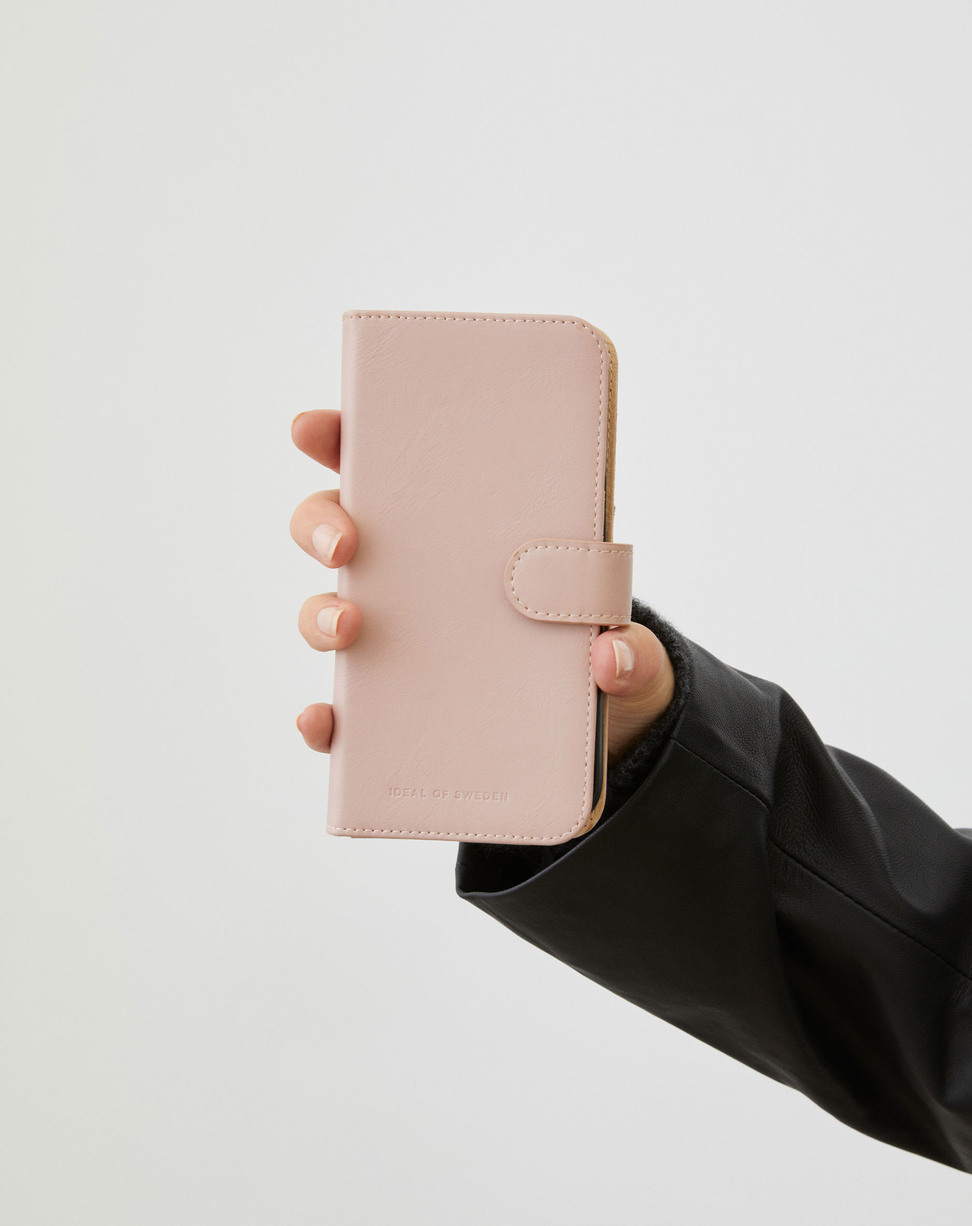 Eine Hand im schwarzen Ärmel hält ein geschlossenes, hellrosa Smartphone-Klappetui vor neutralem Hintergrund.