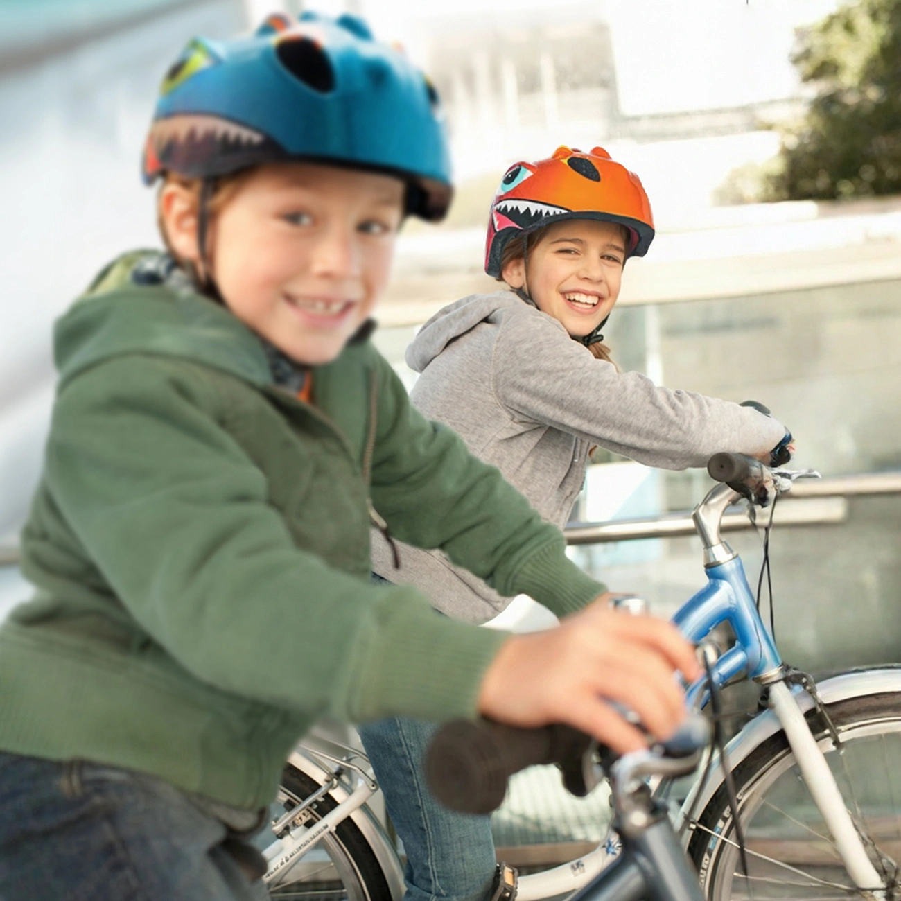 Due bambini sorridenti con elmetti colorati vanno in bicicletta all'aperto.