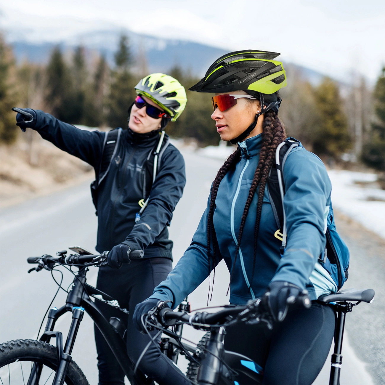Due ciclisti con il casco sono su una strada di montagna mentre uno indica in avanti.