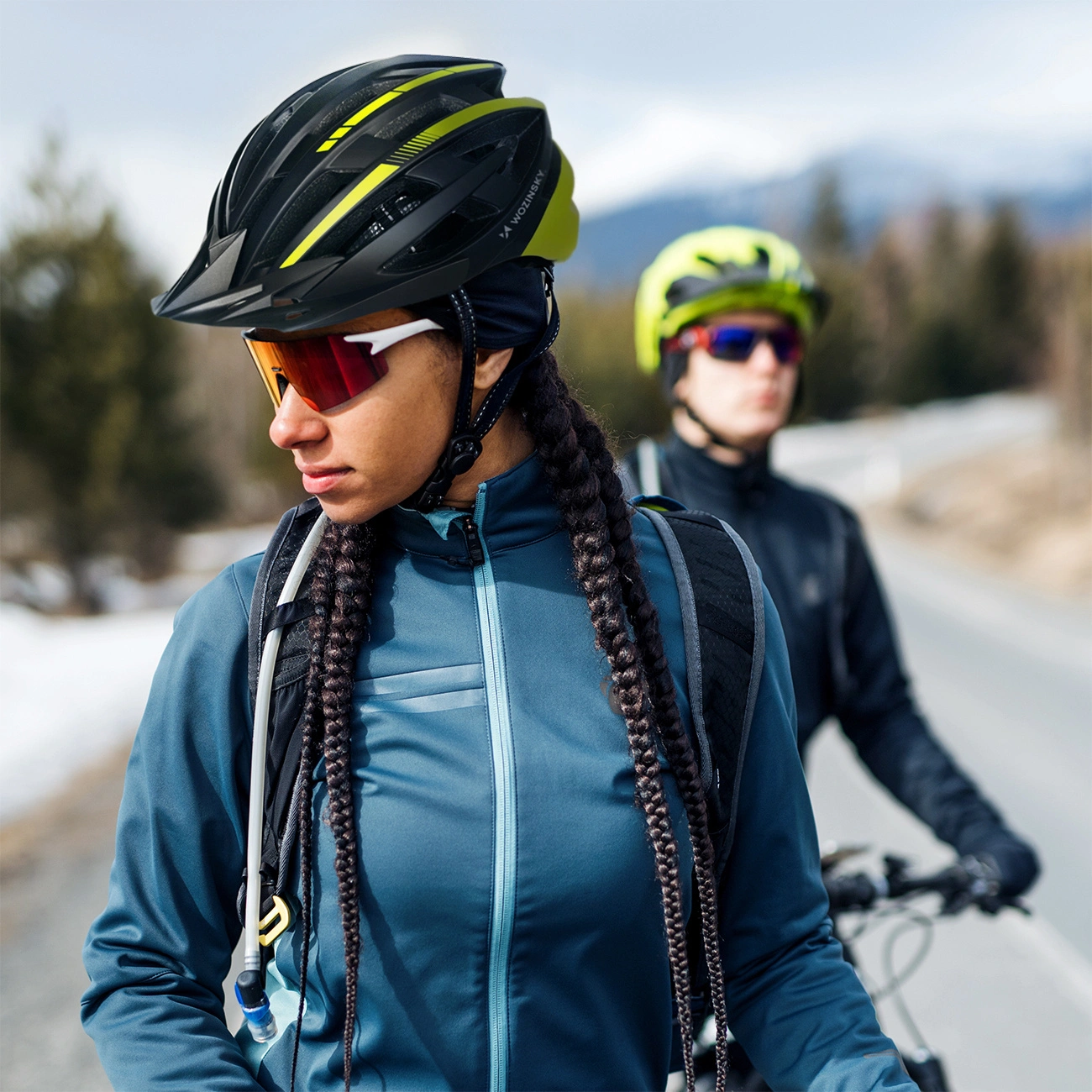 Due ciclisti con casco e occhiali sportivi su una strada all'aperto.