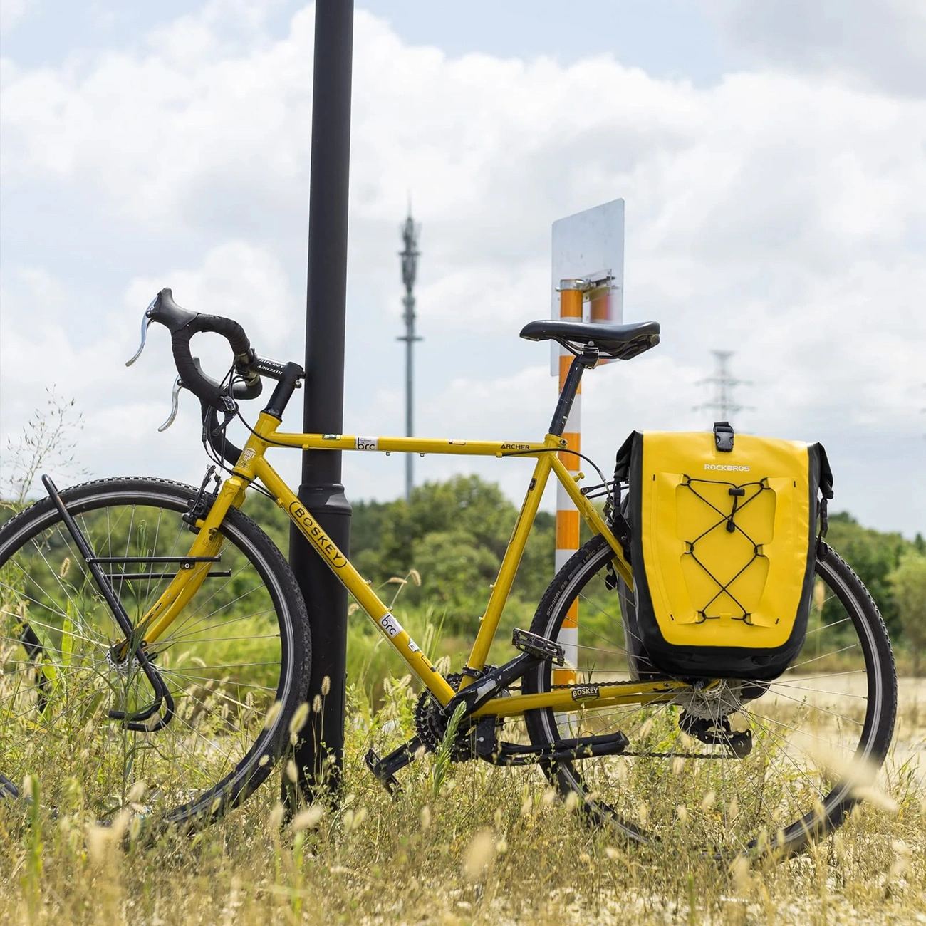 Una bicicletta gialla con borsa laterale parcheggiata su un prato contro un palo.
