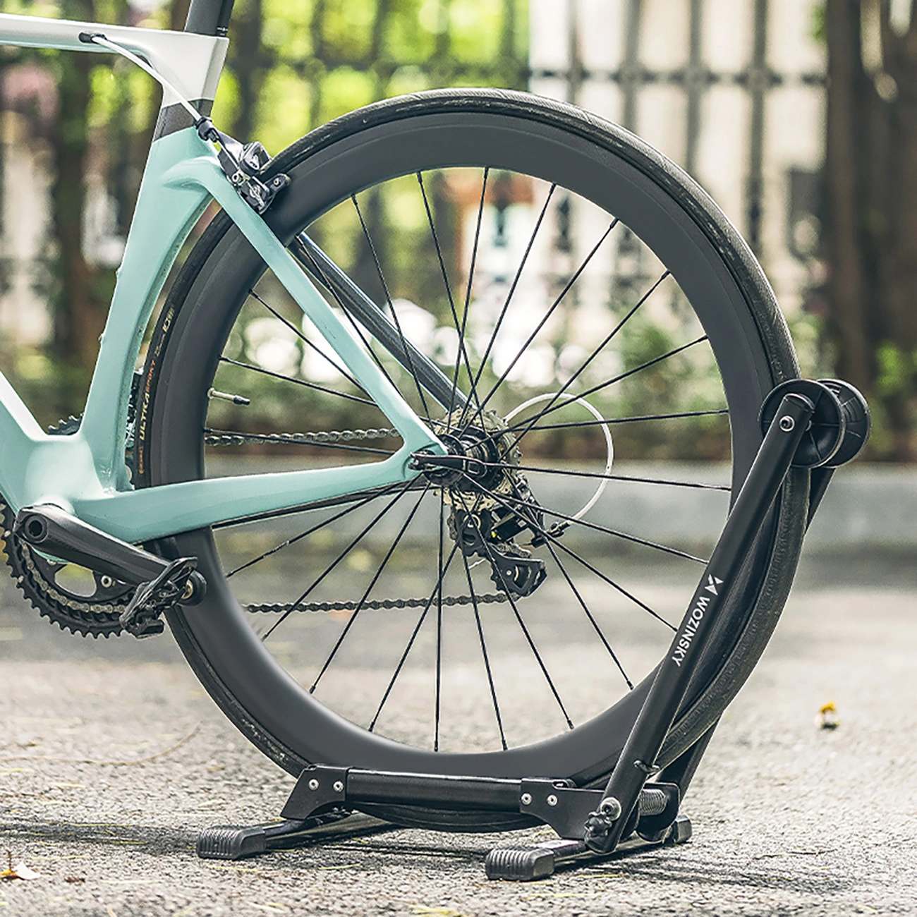 Una bici da corsa verde acqua si appoggia con la ruota posteriore su un supporto nero.