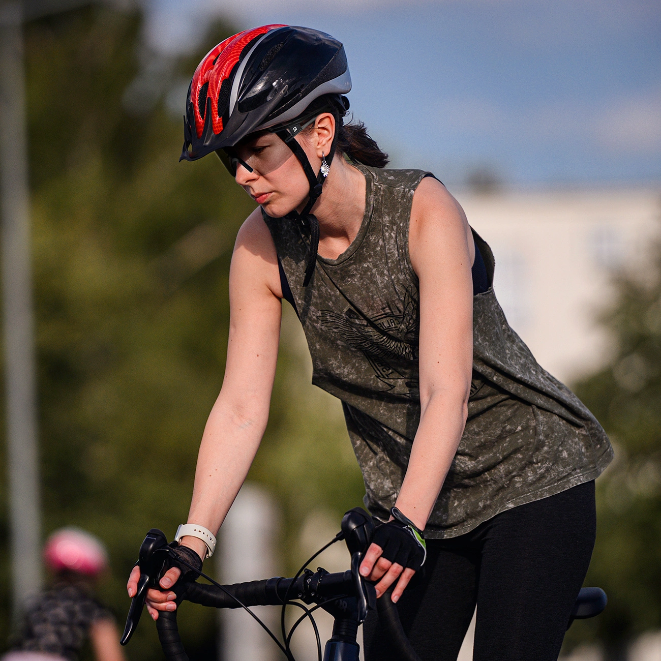 Una donna con casco rosso e nero e canotta verde va in bicicletta all'aperto.