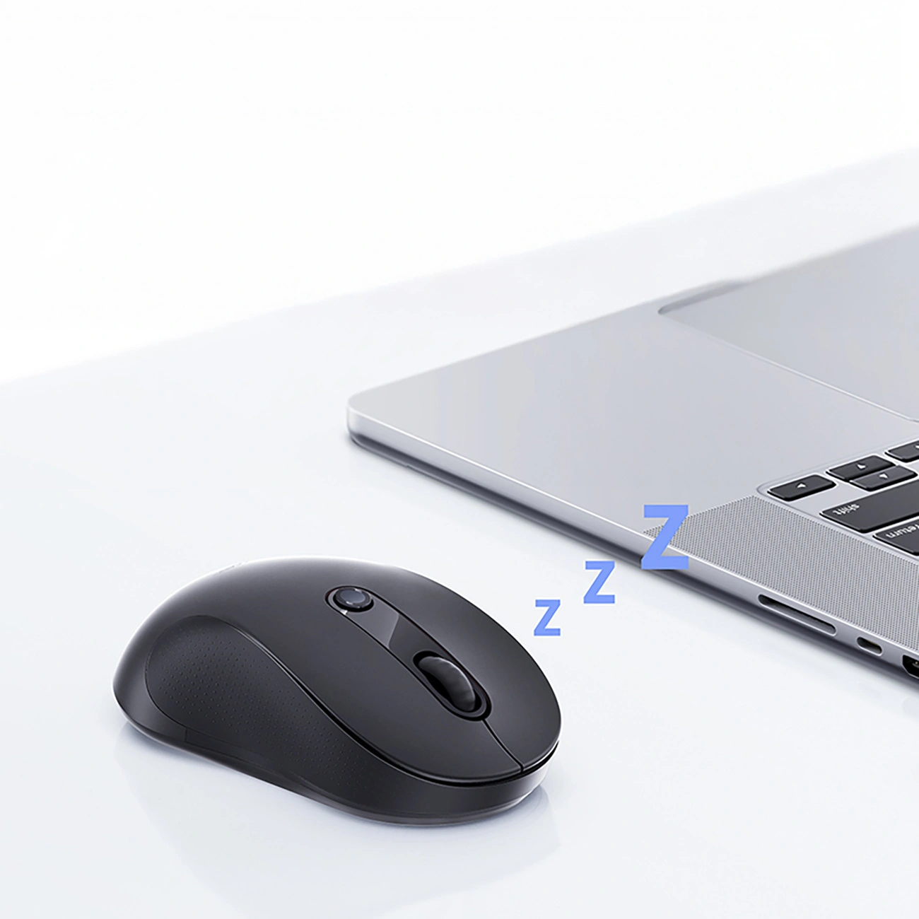 Un mouse per computer nero accanto a un laptop argentato su una superficie bianca, con lettere Z blu.