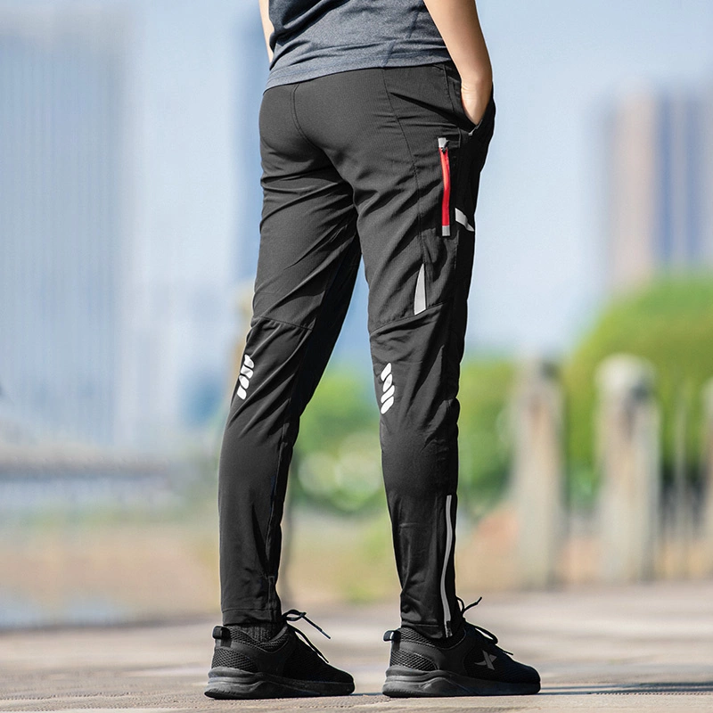 Persona vista di spalle in pantaloni sportivi neri con dettagli riflettenti e scarpe da ginnastica nere all'aperto.