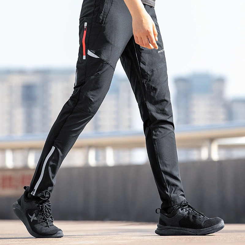 Una persona cammina all'aperto indossando pantaloni sportivi neri con zip rossa e scarpe da ginnastica nere.
