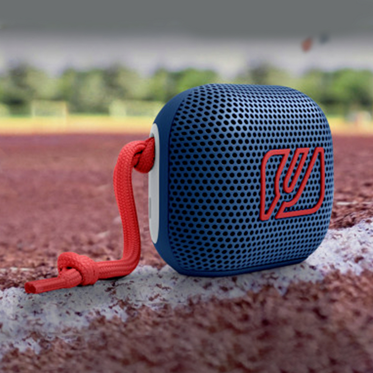 A blue mesh bluetooth speaker with a red cord rests on a red running track.