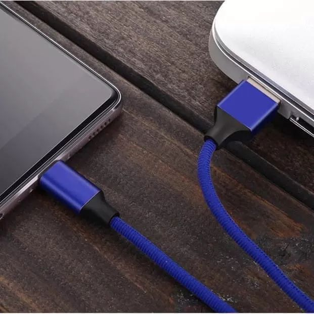 Niebieski kabel ładujący łączy smartfon z laptopem na drewnianej powierzchni.