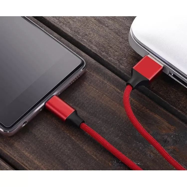 Czerwony pleciony kabel USB łączy smartfon z laptopem na drewnianej powierzchni.
