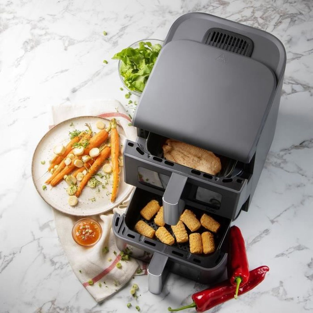 Friteuse sans huile grise à double tiroir sur marbre avec viande et croquettes, carottes et salade.
