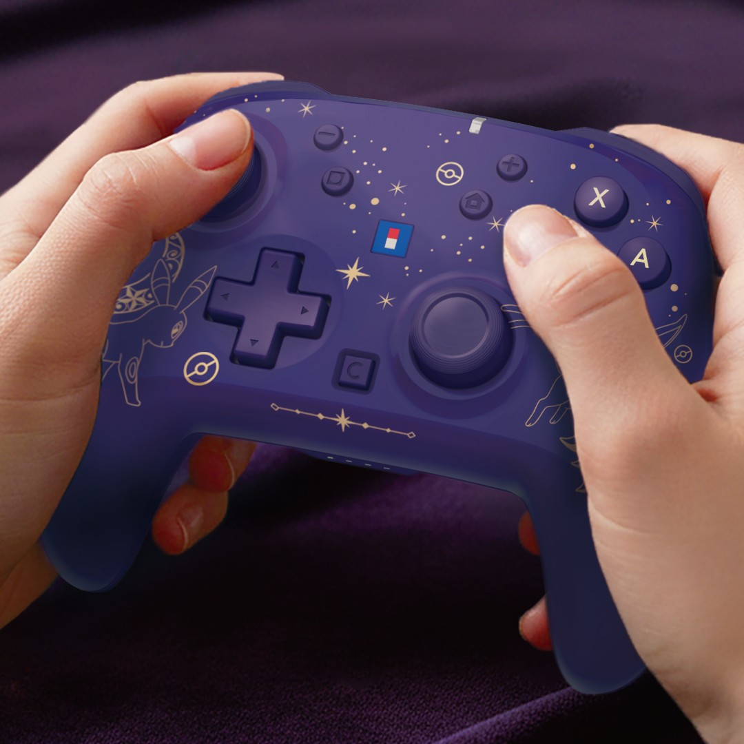Hände halten einen violetten kabellosen Controller mit goldenen Himmelsmustern vor dunklem Hintergrund.