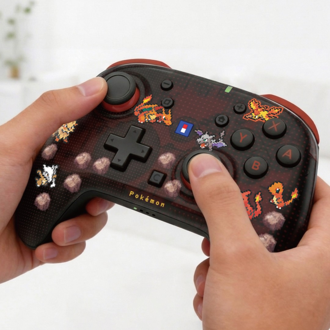 Ein Hände halten einen schwarz-roten Pokémon-Gamepad mit Pixel-Art-Motiven gegen einen hellen Hintergrund.