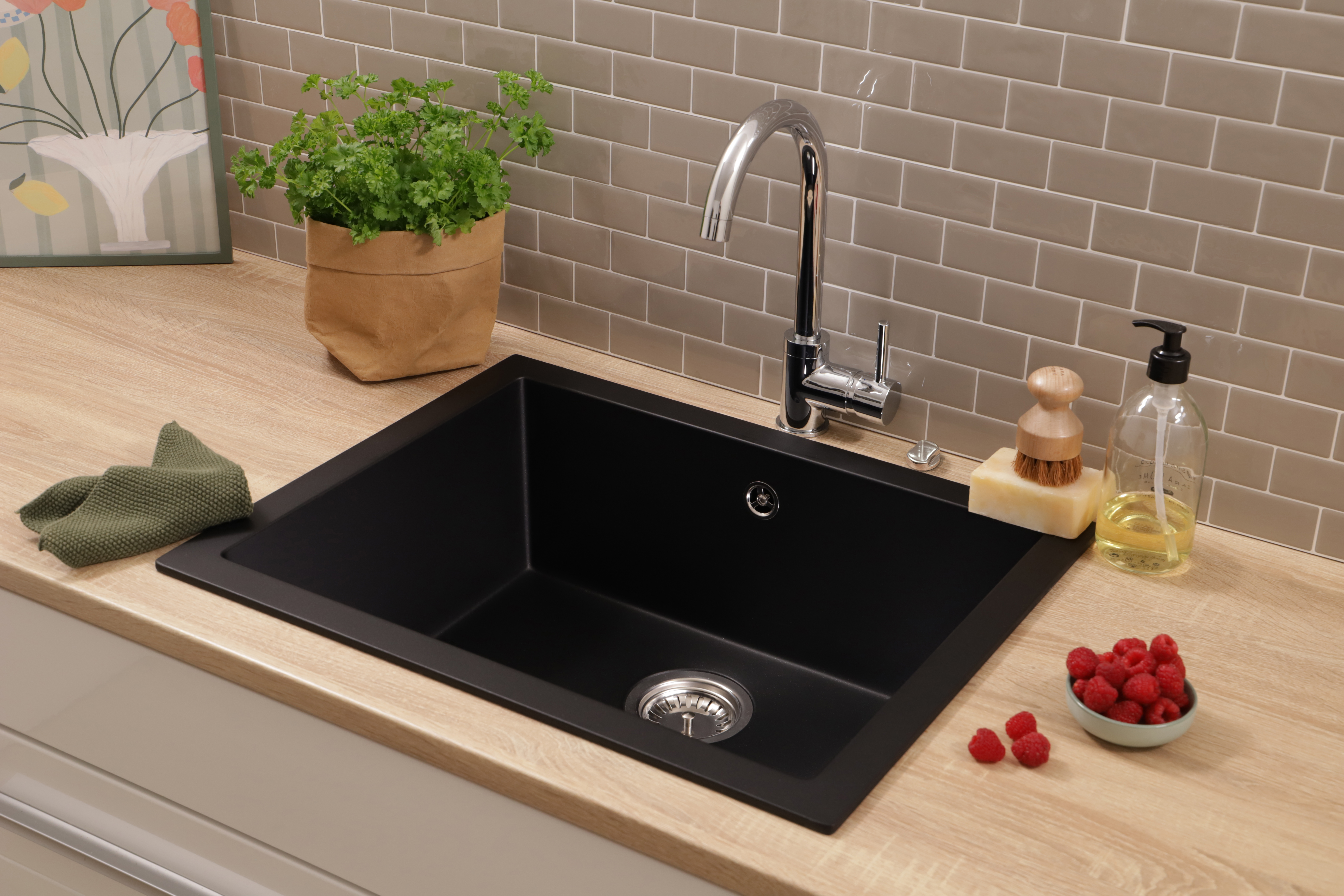 Ein schwarzes Spülbecken mit Chromarmatur auf einer Holzarbeitsplatte, umgeben von Kräutern, Seife und Himbeeren.