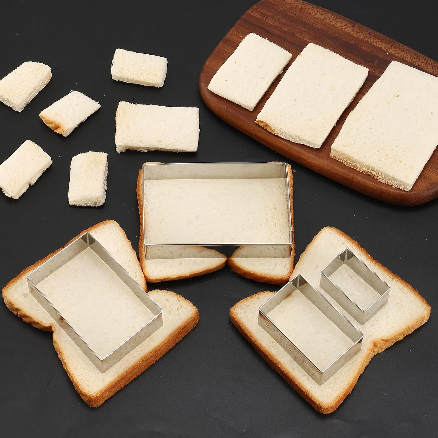 Geschnittenes Brot und Metallformen auf einem dunklen Tisch, begleitet von einem Holzbrett.