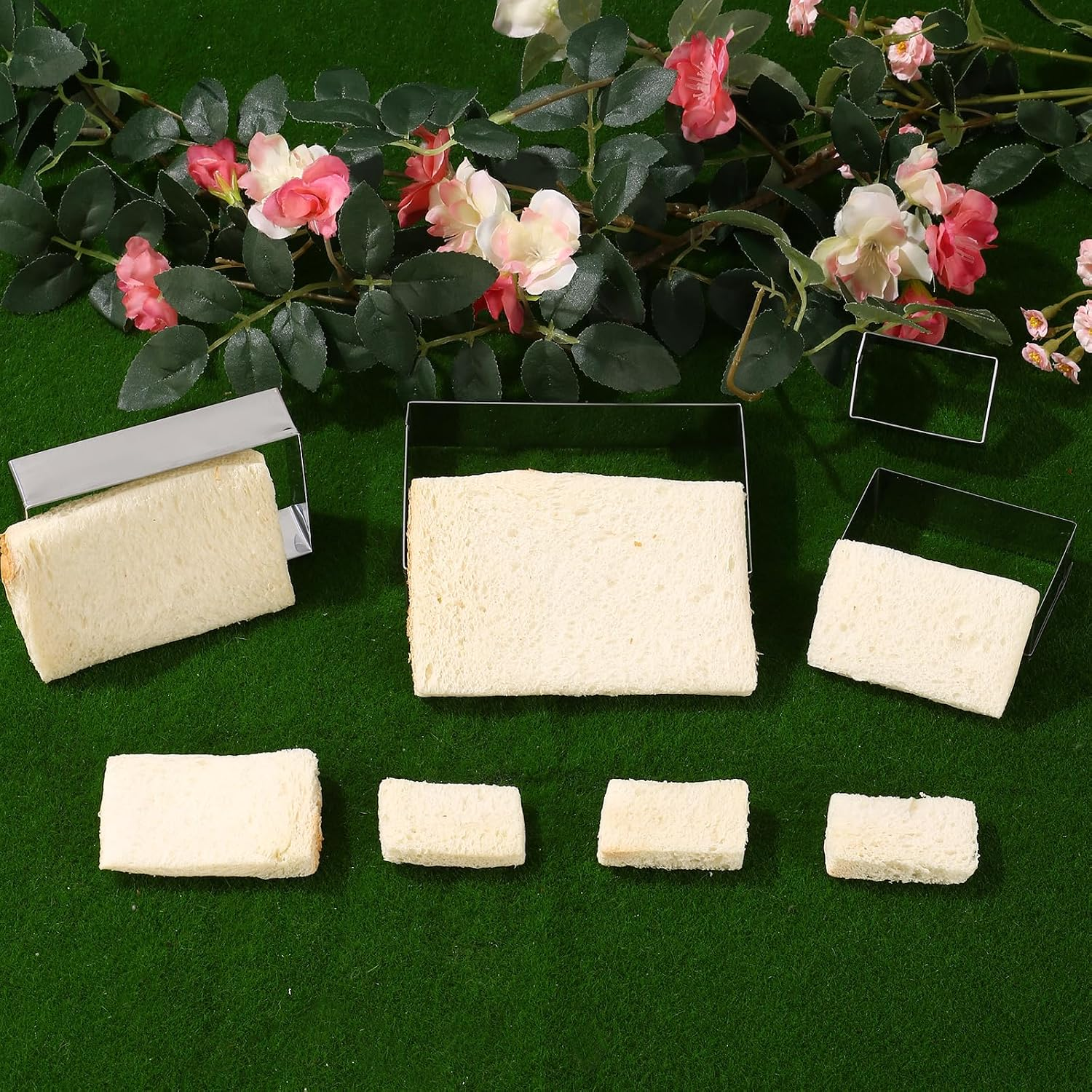 Verschiedene rechteckige Weißbrotscheiben und Metallformen liegen auf grünem Untergrund vor Rosen.