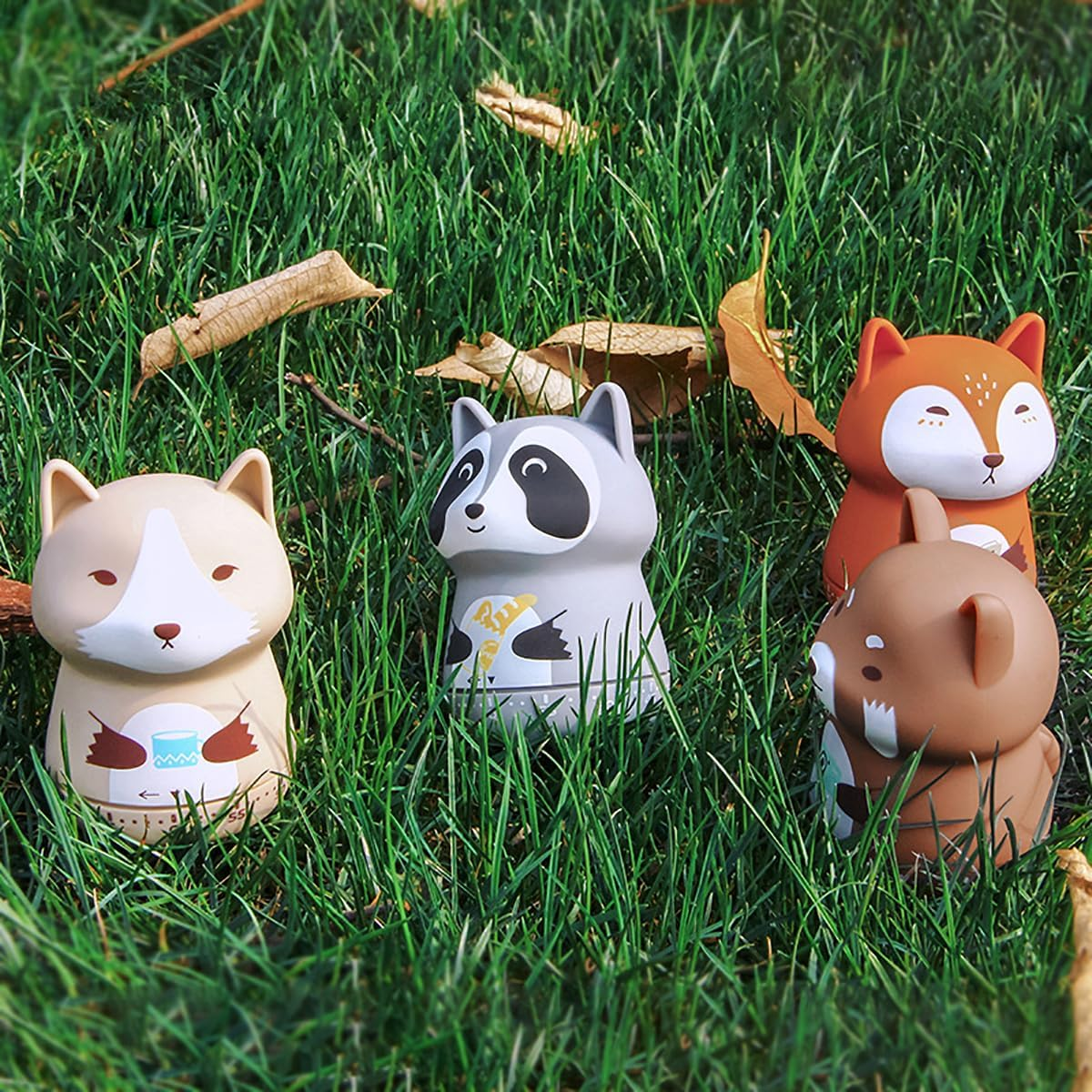 Vier Tierfiguren, darunter ein Waschbär und ein Fuchs, stehen im grünen Gras.