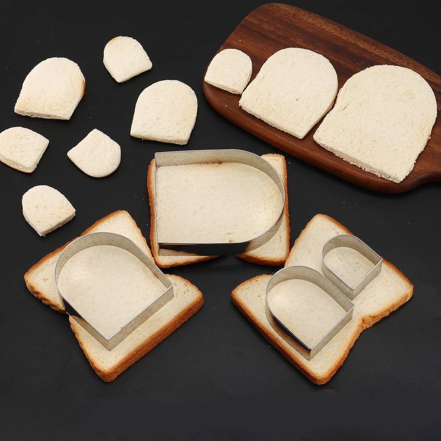 Brotstücke und Metallförmchen auf einem dunklen Tisch, dazu ein Holzbrett.