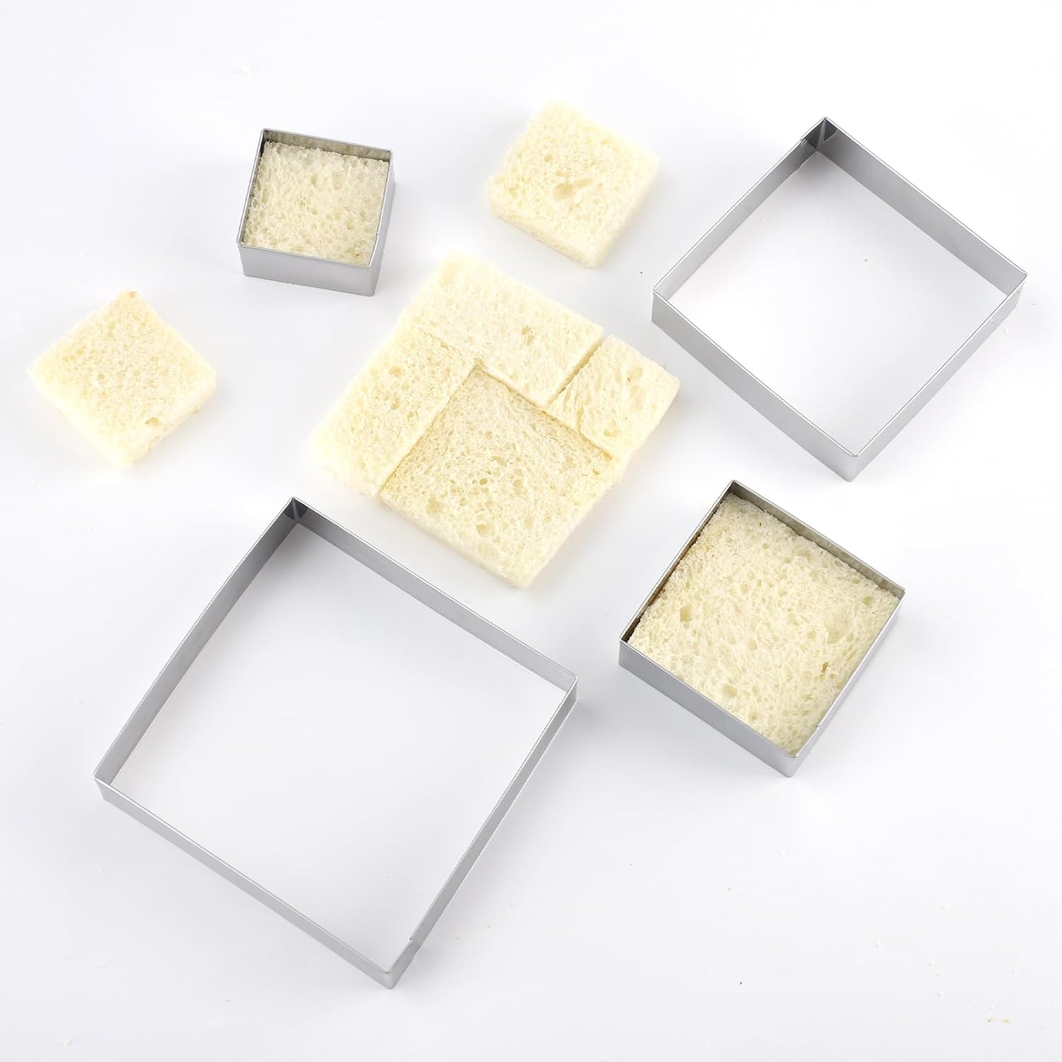 Quadratische Metallformen und geschnittene weiße Brotwürfel auf weißem Hintergrund.