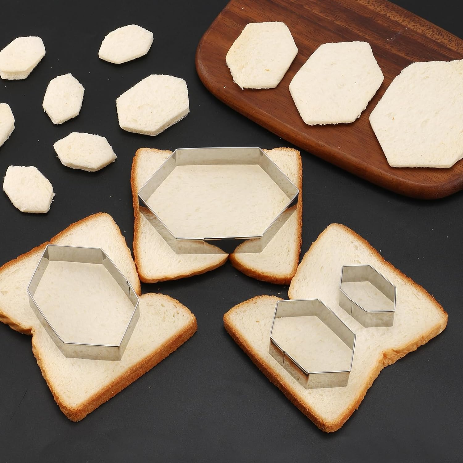 Sechseckige Keksformen aus Metall schneiden Formen aus weißen Brotscheiben auf einer dunklen Fläche.