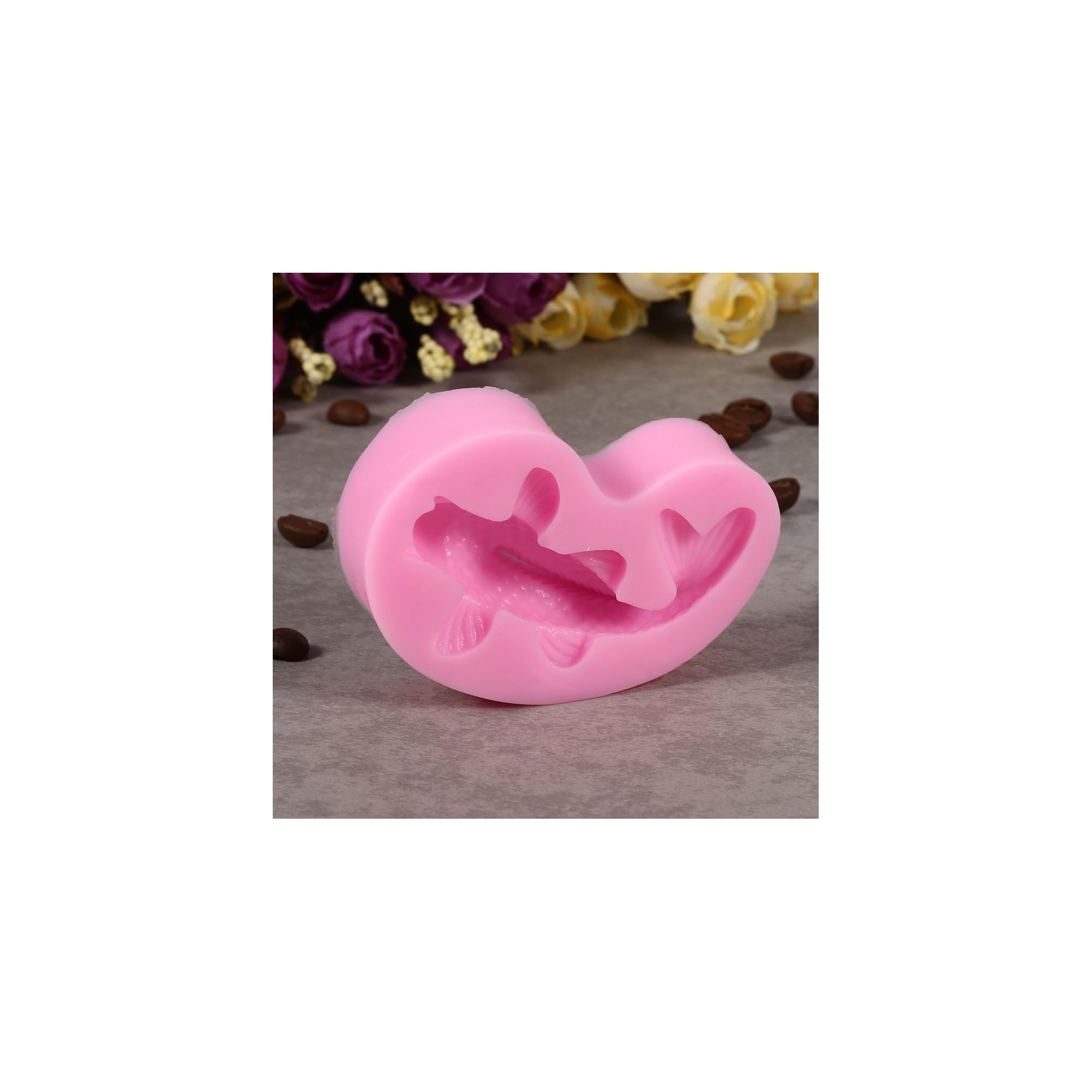 Eine rosa Silikonform eines Fisches liegt auf grauer Oberfläche mit Kaffeebohnen und Blumen im Hintergrund.