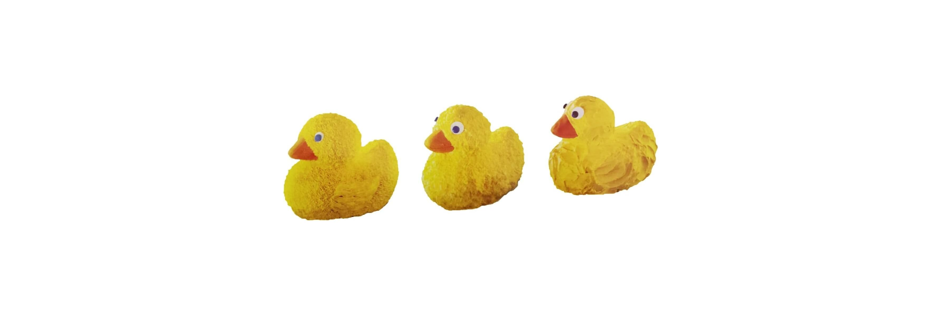 Drei kleine gelbe Entenfiguren stehen in einer Reihe vor weißem Hintergrund.