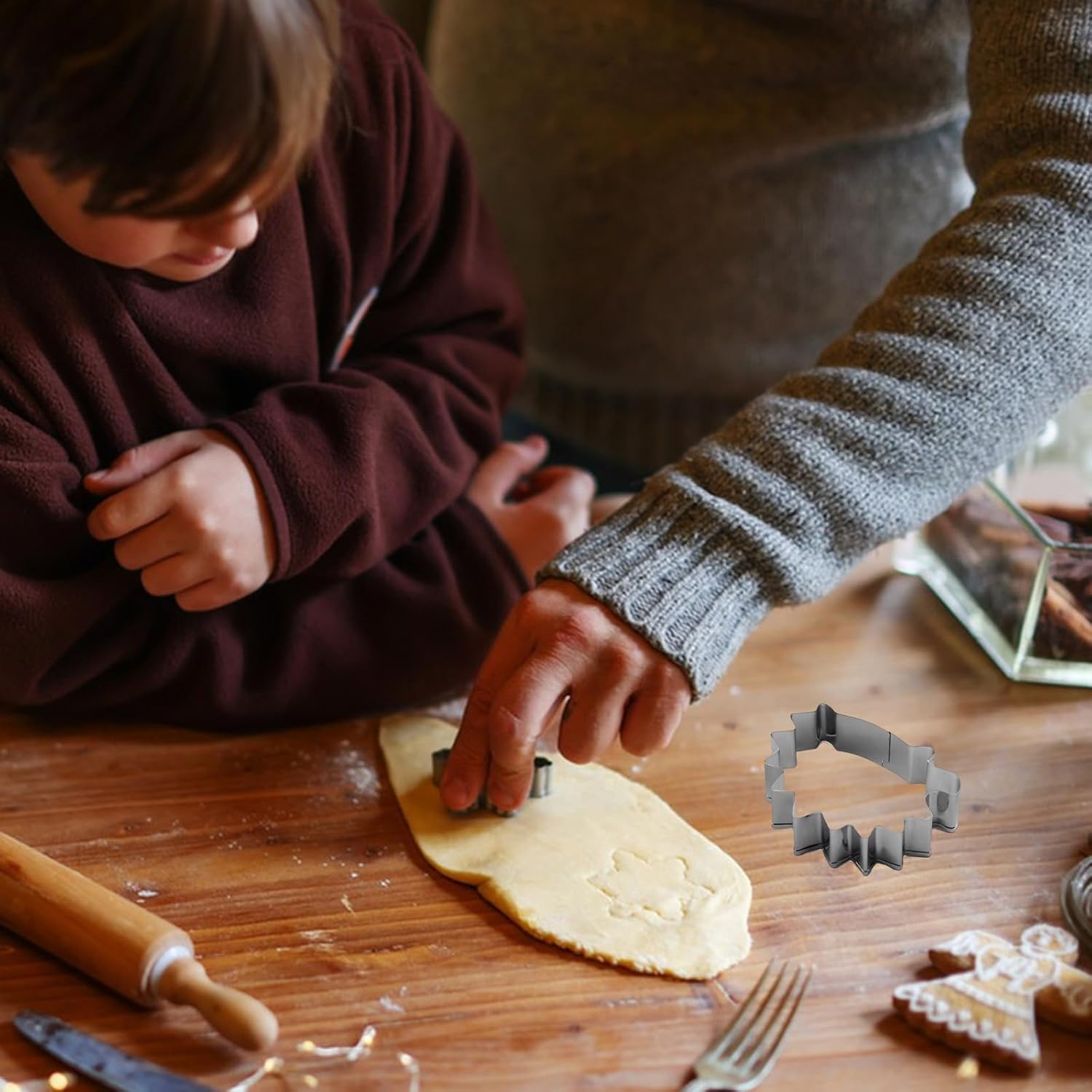 Ein Kind und ein Erwachsener schneiden Plätzchenteig mit einem Ausstecher auf einem Holztisch.