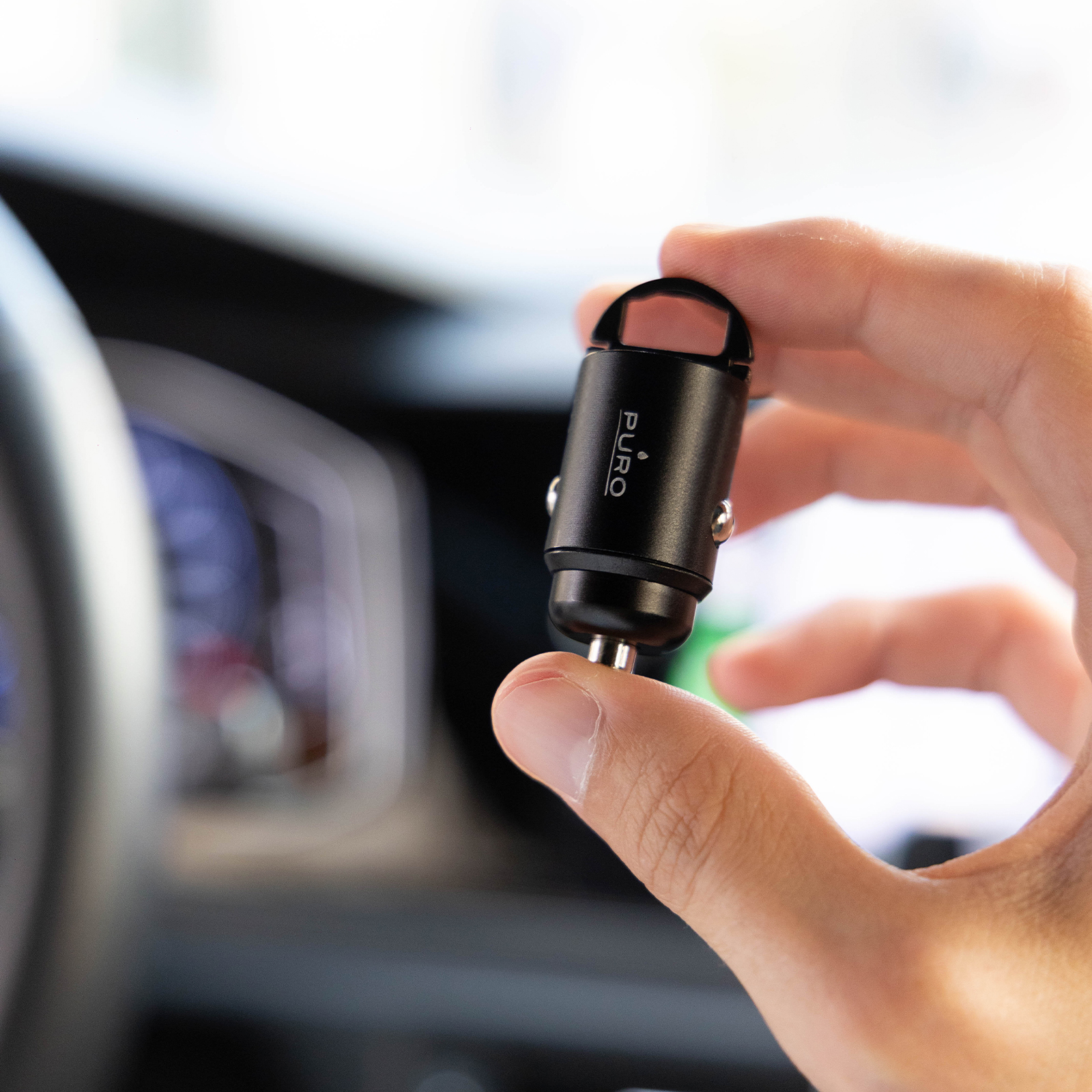 Una mano tiene un piccolo caricabatterie per auto Puro nero davanti agli interni di un'auto.