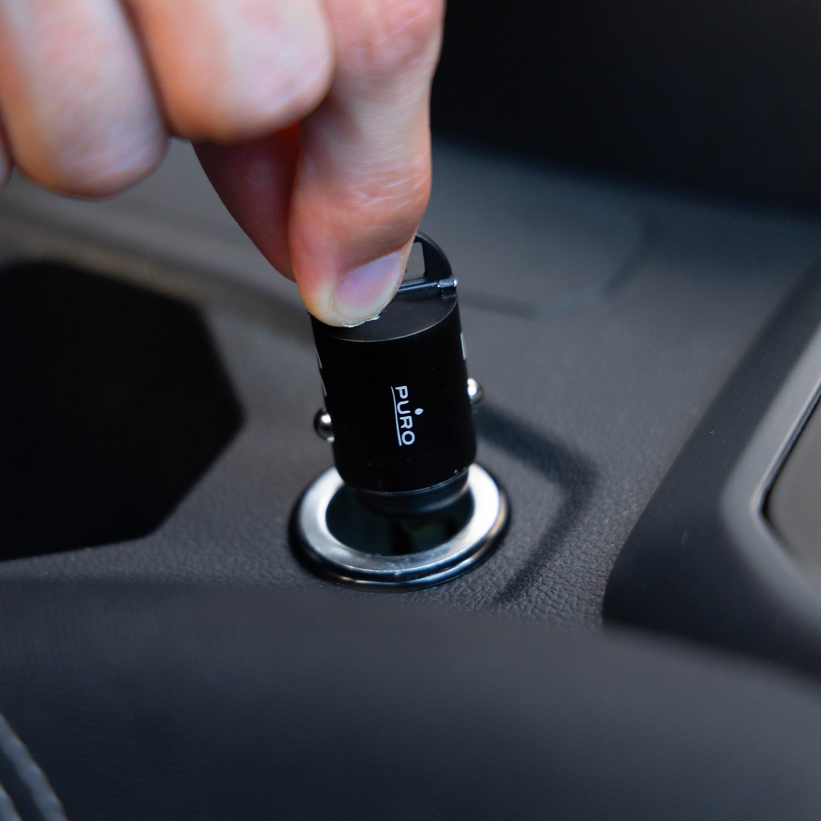 Una mano inserisce un caricabatterie per auto nero PURO nell'accendisigari.