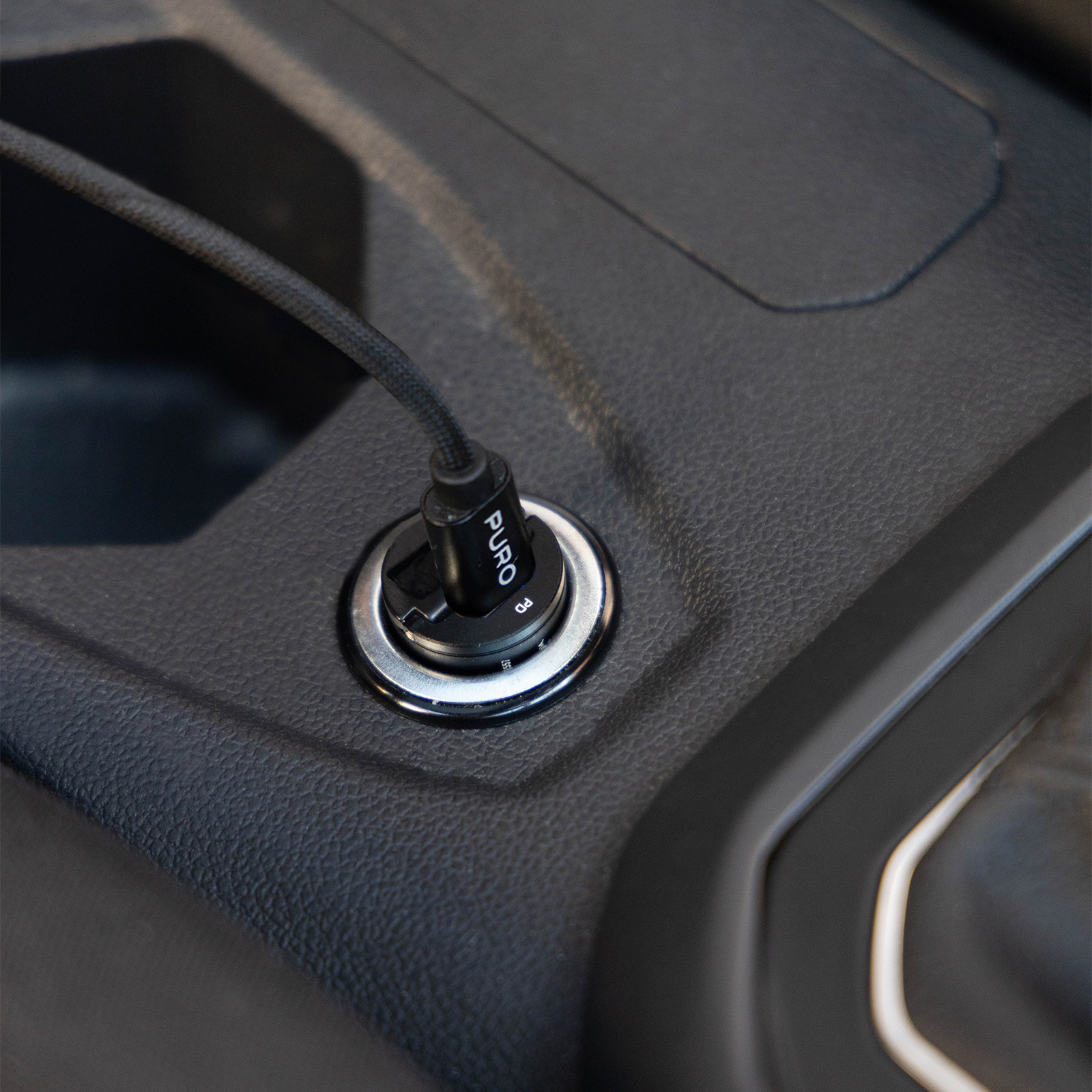 Un caricabatterie per auto nero con logo PURO è inserito nella presa della console centrale.