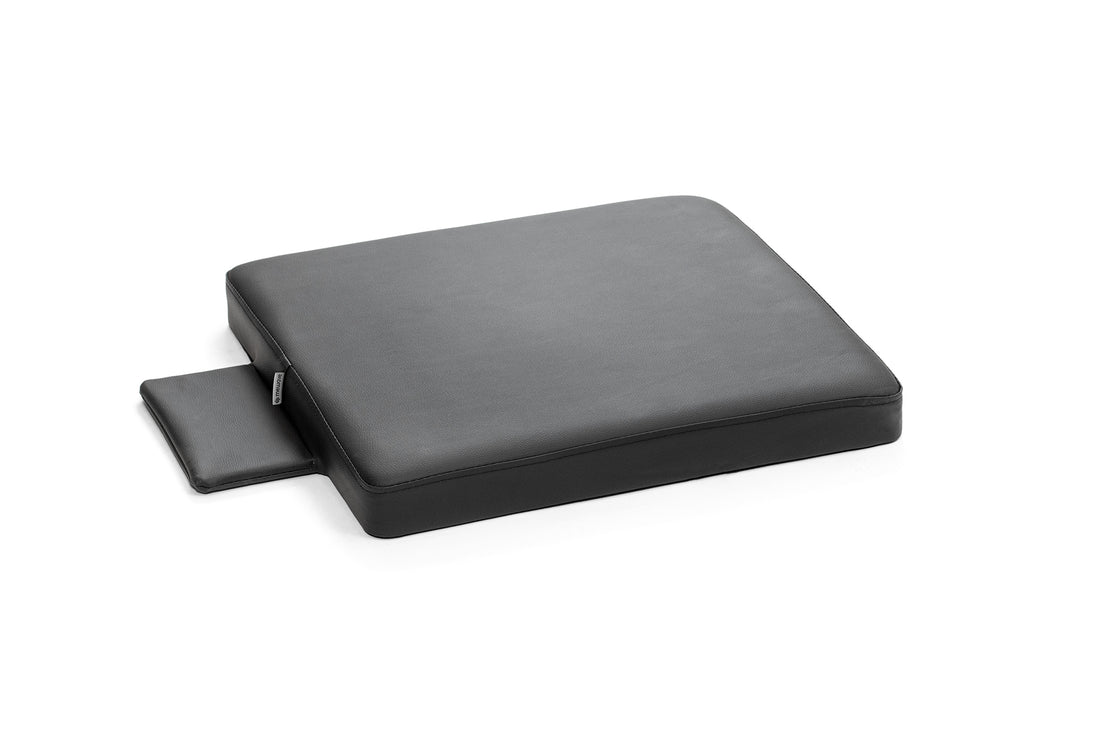 Un cojín grande de cuero negro con una pequeña extensión en el lateral sobre fondo blanco.