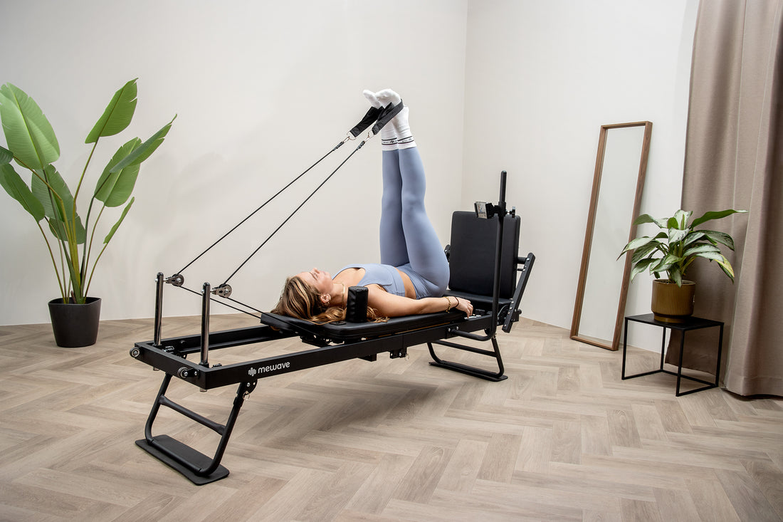Una mujer en ropa deportiva hace ejercicio en una máquina reformer de pilates negra con correas.