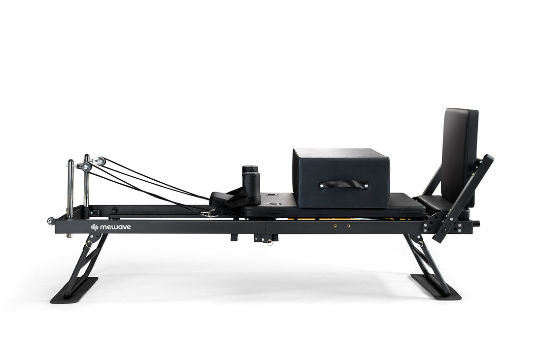 Un reformer de pilates negro con caja y barra de pies ajustable sobre fondo blanco.