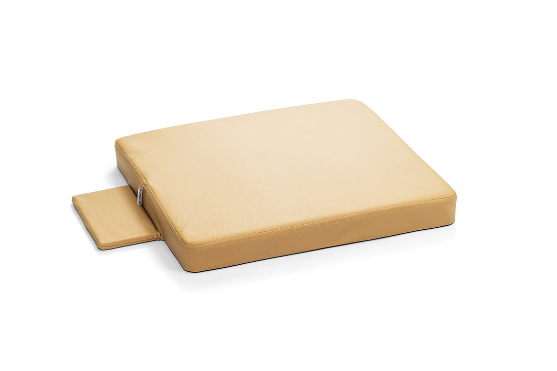 Un cojín terapéutico beige sobre fondo blanco con una pequeña almohadilla adjunta al lado.