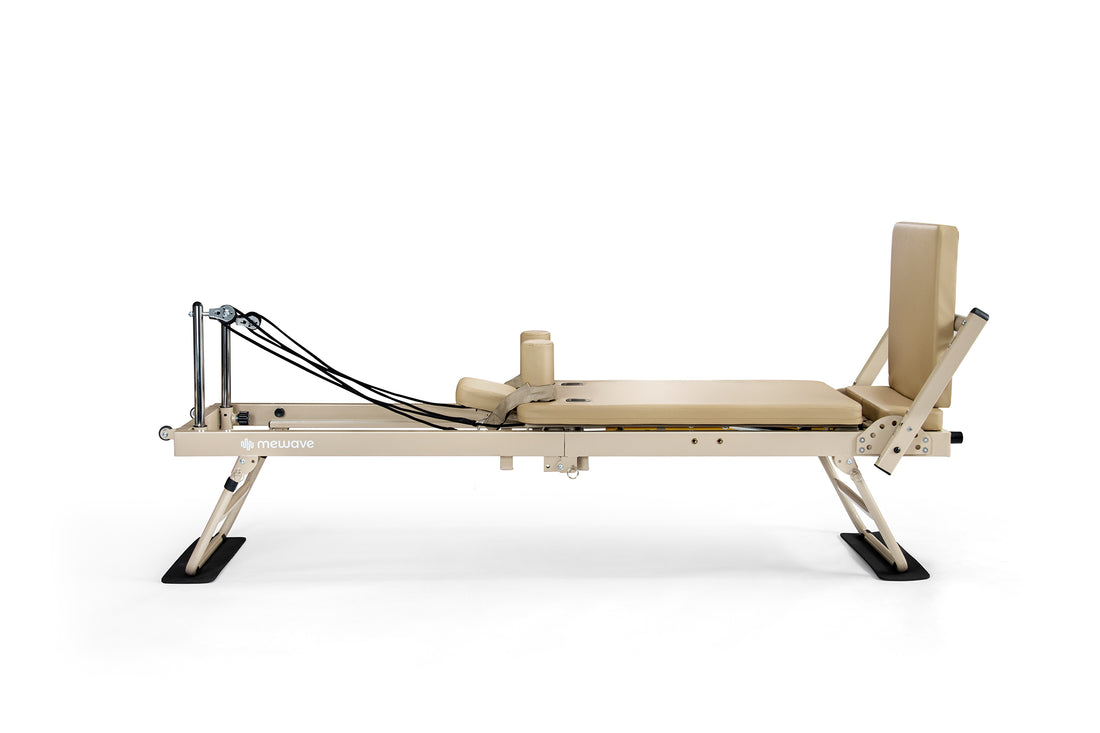 Una máquina reformer de pilates beige con correas negras y barra de pies sobre fondo blanco.