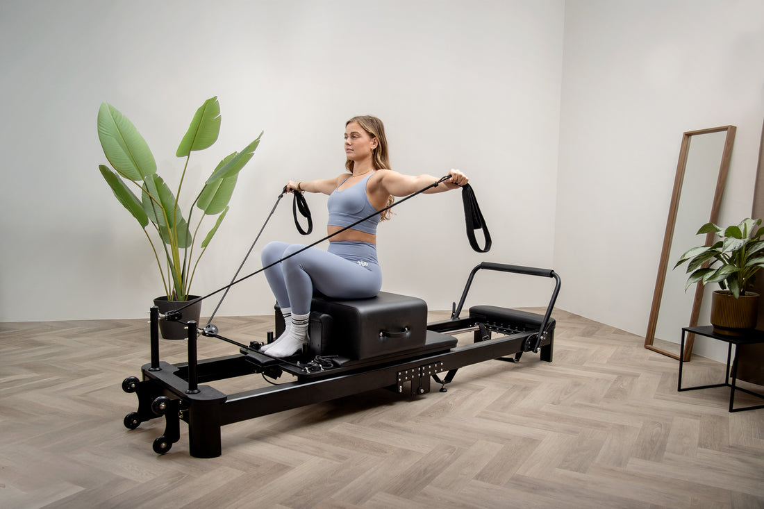 Una mujer en ropa deportiva azul usa una máquina de pilates en una habitación luminosa con plantas.