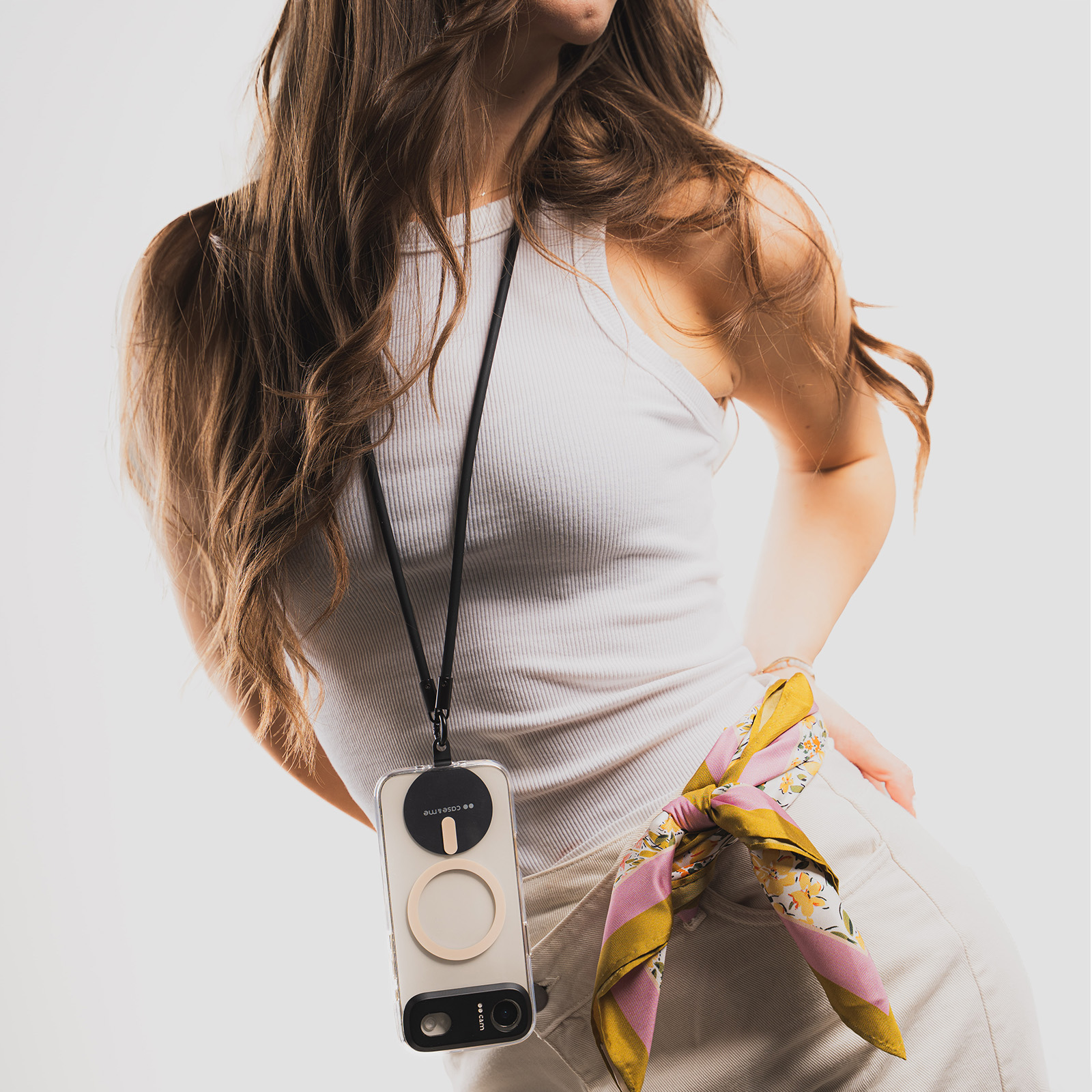 Una mujer con top blanco y falda clara lleva un móvil con cordón negro y un pañuelo colorido.