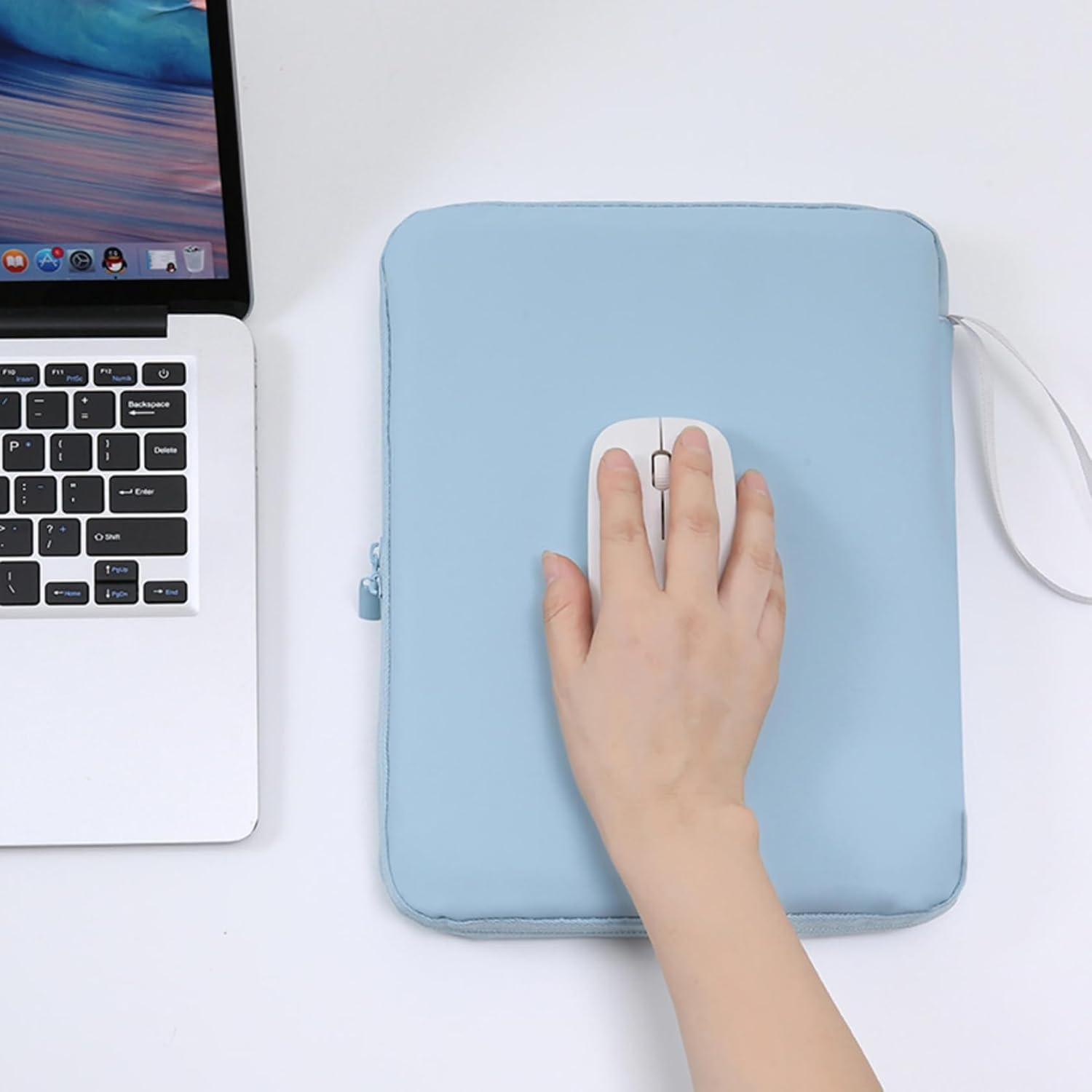 Eine Hand benutzt eine weiße Computermaus auf einer hellblauen Laptoptasche neben einem Laptop.