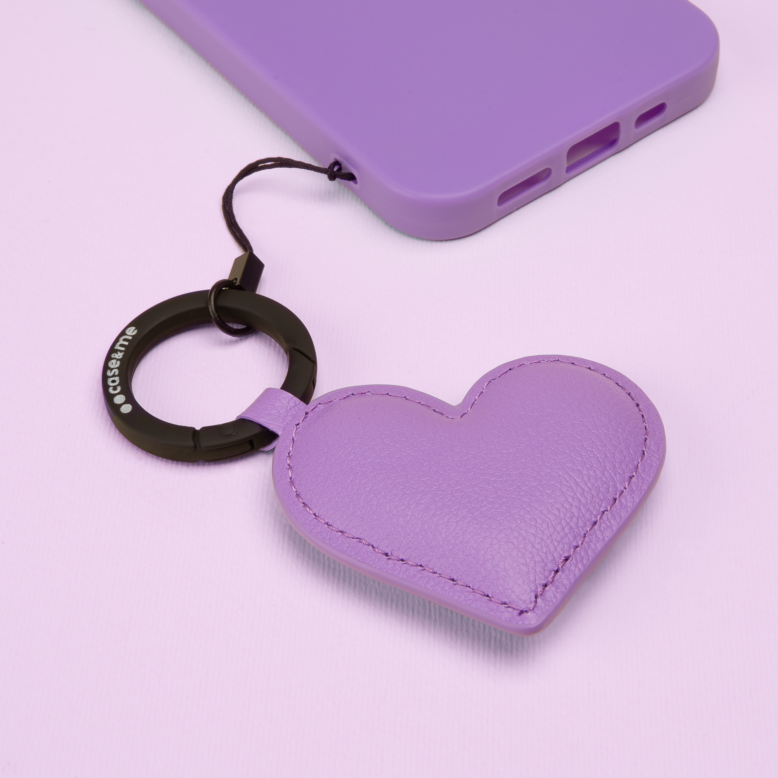 Una funda de móvil morada descansa sobre un fondo morado junto a un llavero en forma de corazón.