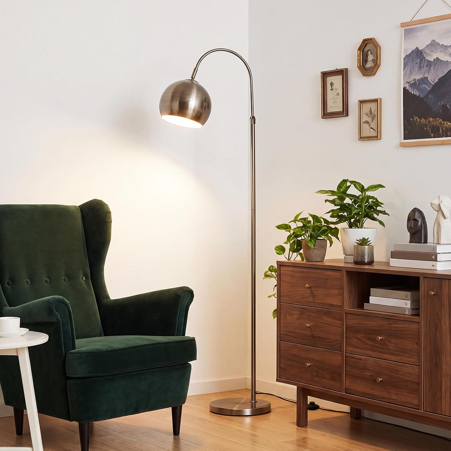 Un sillón verde, una lámpara de pie arqueada y un aparador de madera con plantas en una sala luminosa.