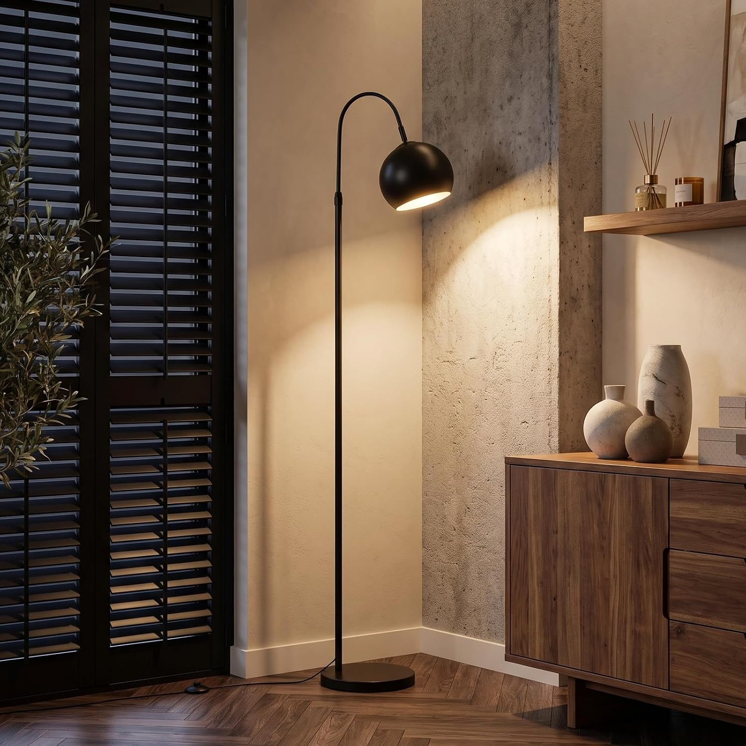 Una lámpara de pie arqueada negra se encuentra en una esquina, iluminando una pared junto a un mueble de madera con floreros.