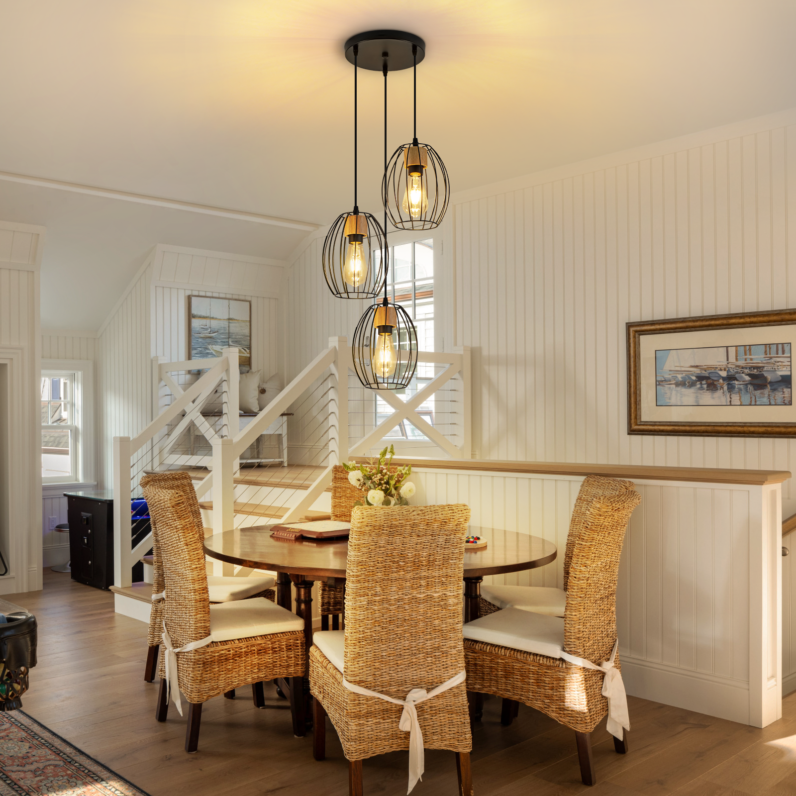 Comedor con mesa de madera y sillas de ratán, iluminado por una lámpara colgante de tres luces ante una pared blanca.