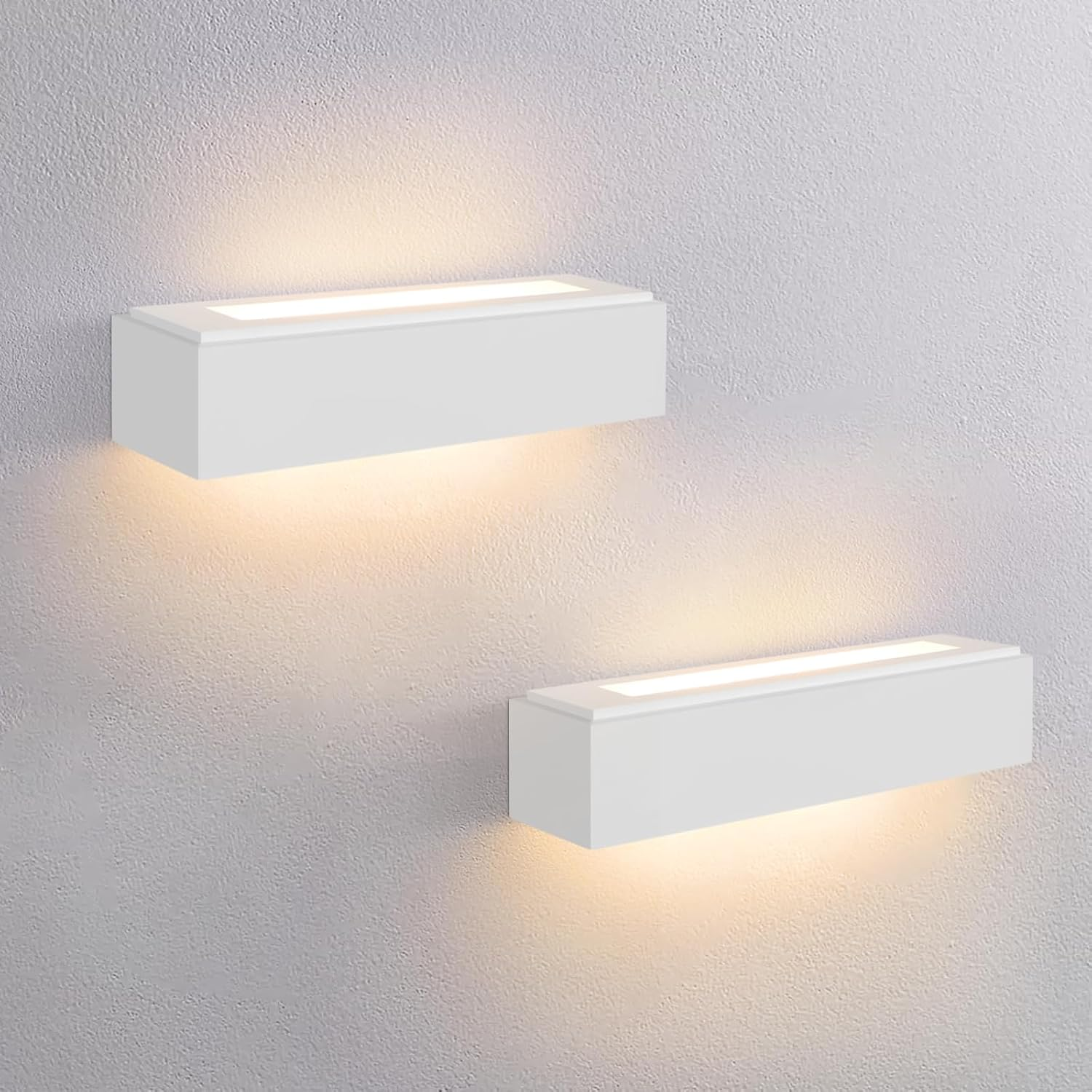 Dos apliques de pared blancos emiten luz cálida hacia arriba y hacia abajo en una pared clara.