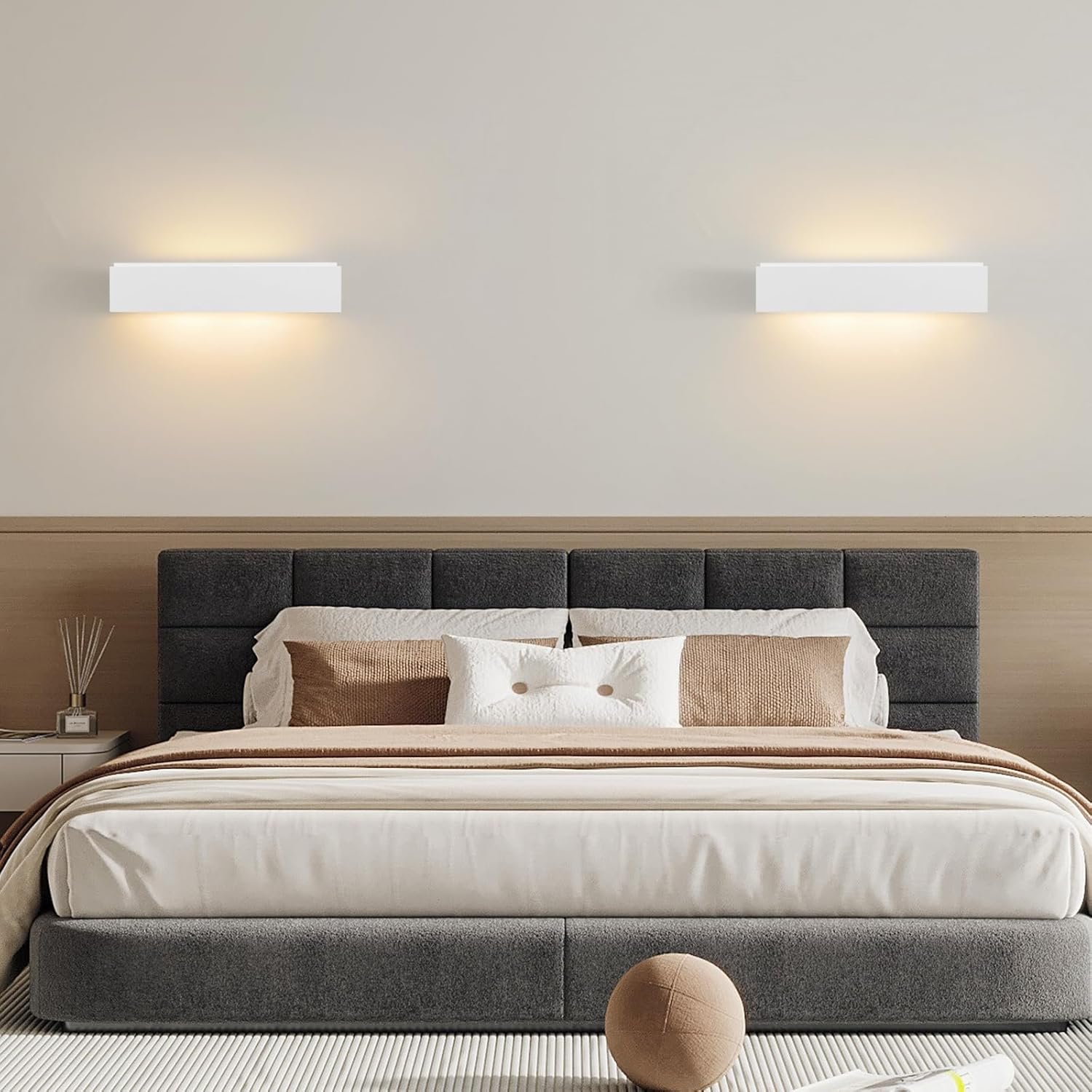 Un dormitorio moderno tiene una cama gris oscura con cojines neutros y dos apliques de pared.