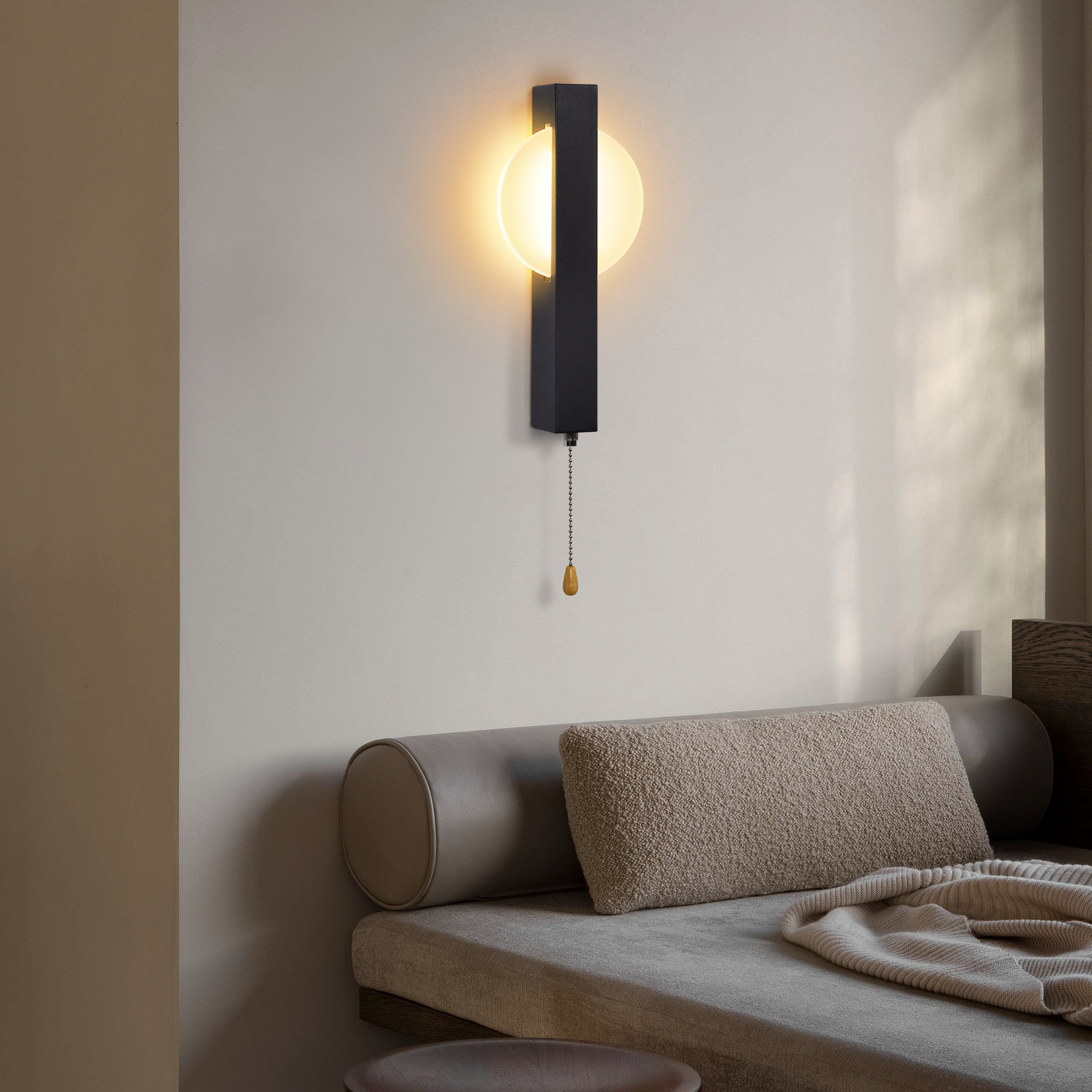 Una moderna lámpara de pared negra con luz redonda está montada sobre un sofá beige con cojines.