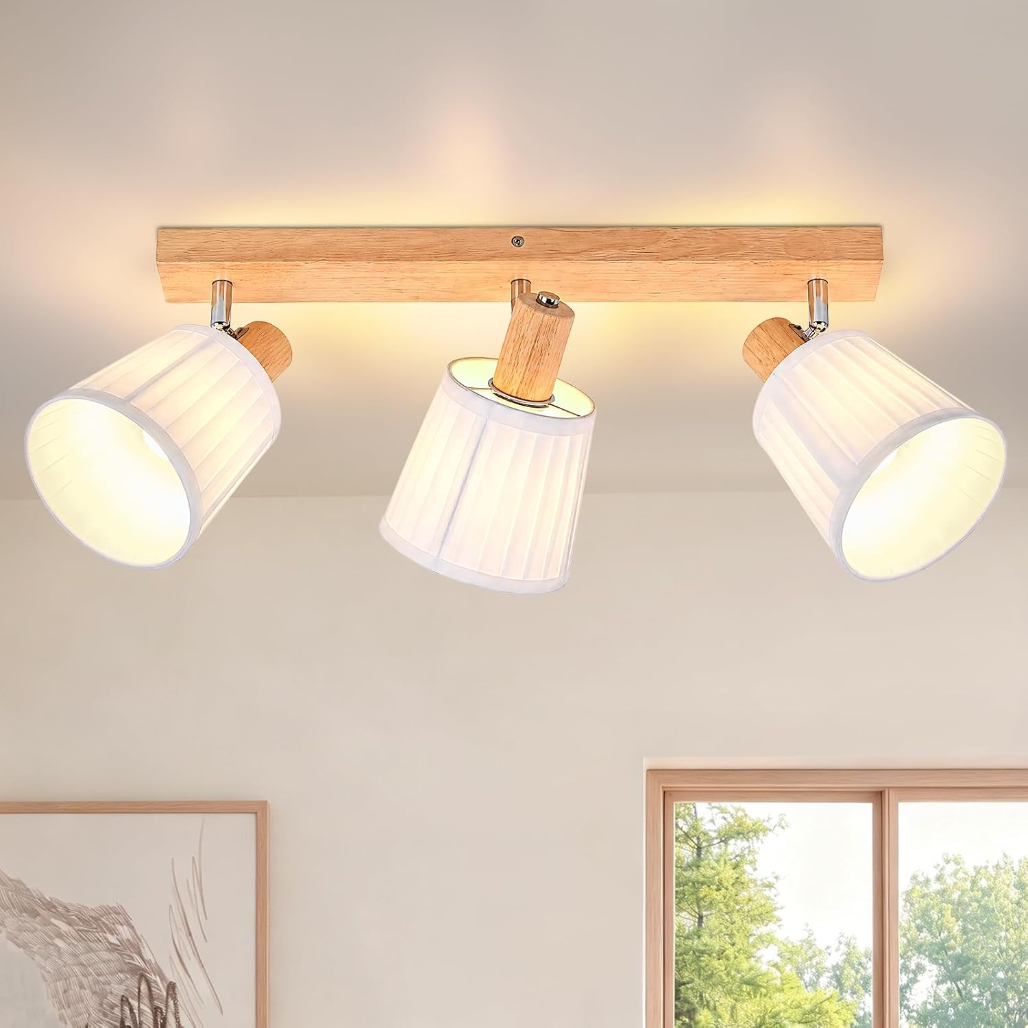 Una lámpara de techo de madera con tres pantallas plisadas de tela blanca montadas en una base larga sobre una pared lisa.